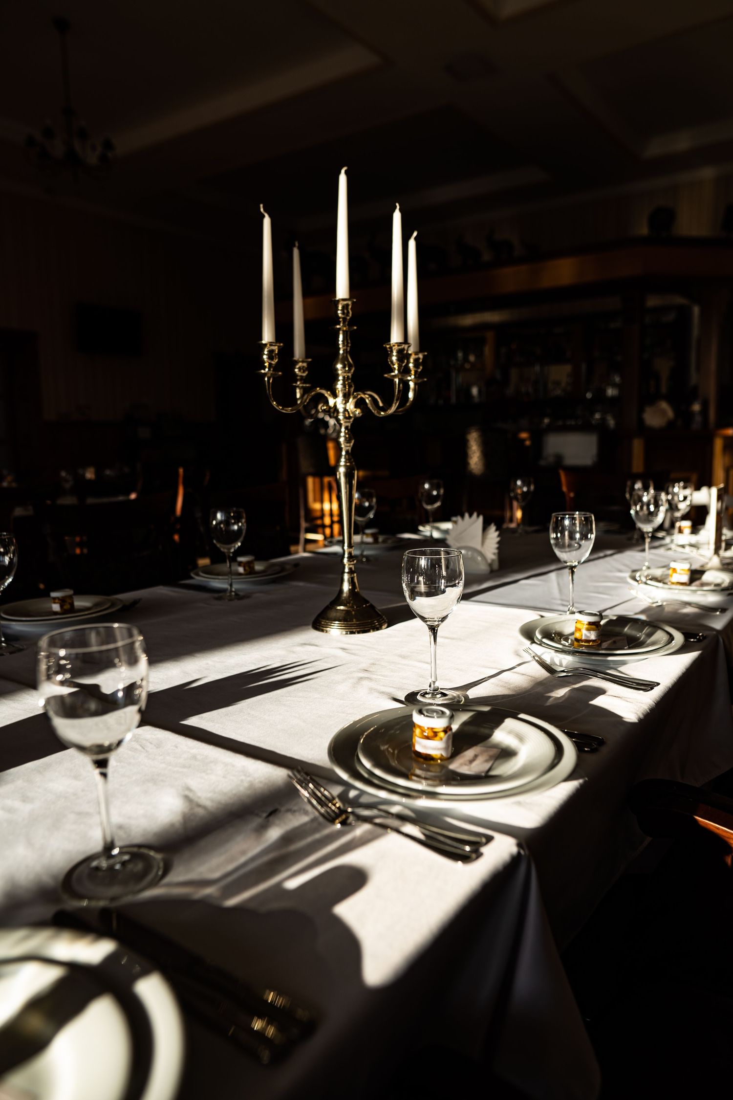 Elegant table settings with white linens, wine glasses, and candlesticks cast dramatic shadows in a dimly lit restaurant.