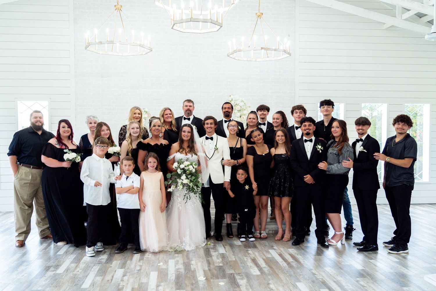 Wedding party members pose together in a bright white venue wearing formal black and white attire.