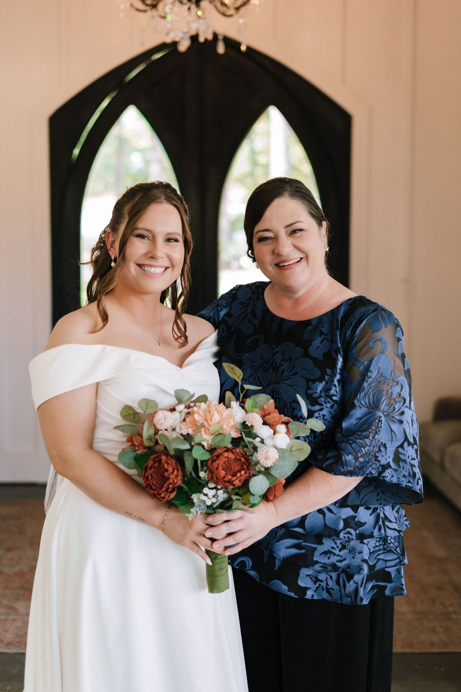 Two wedding attendants pose together in a white dress and navy lace gown holding floral bouquets.
