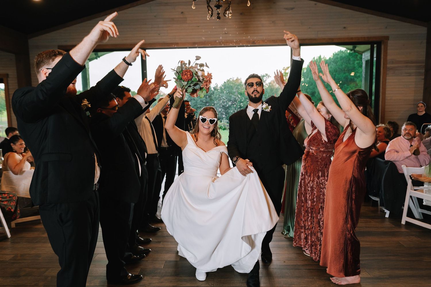 Wedding party dances and celebrates during reception in rustic venue.