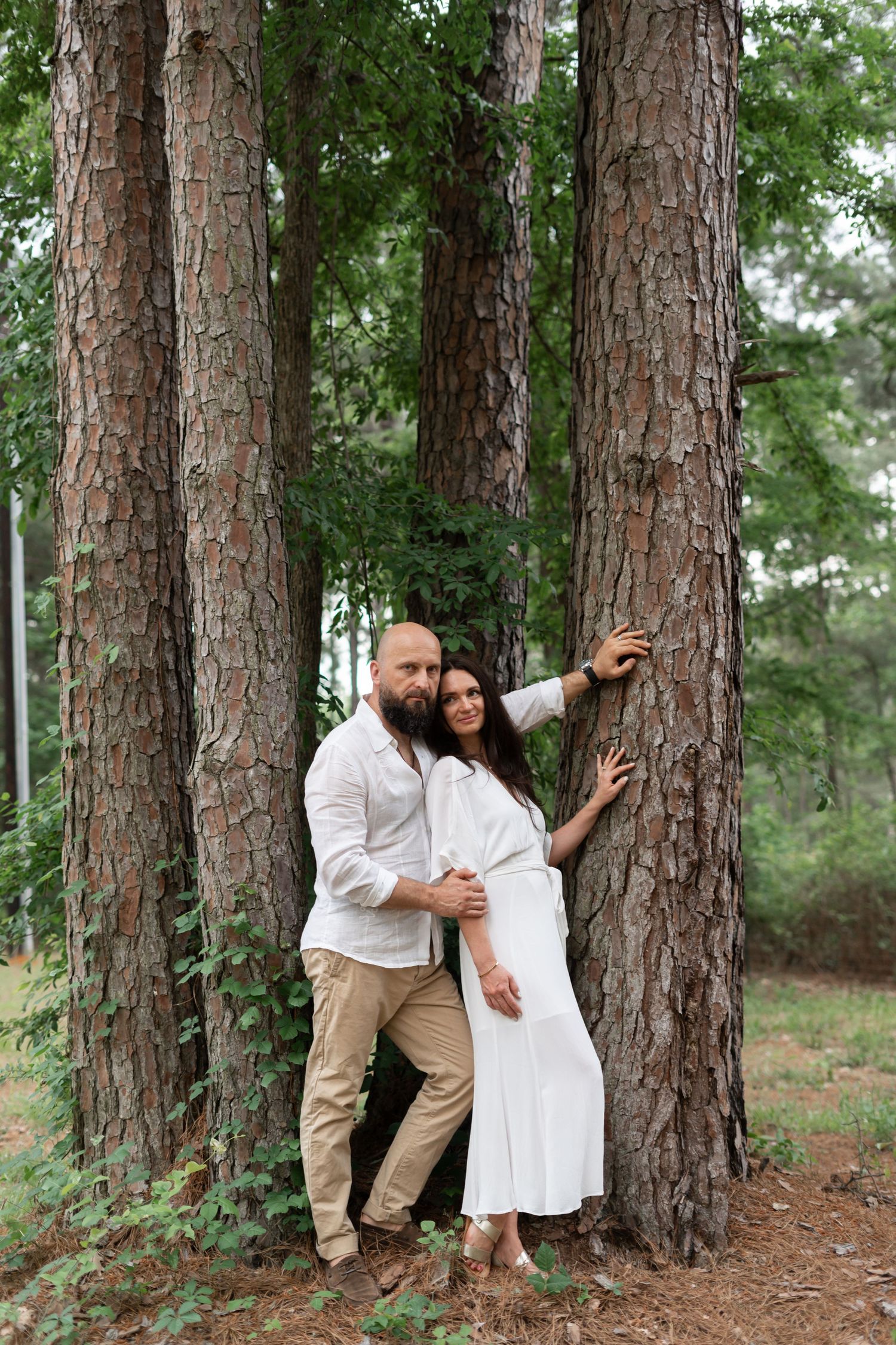 Playful engagement photos captured between tall pine trees in natural lighting.