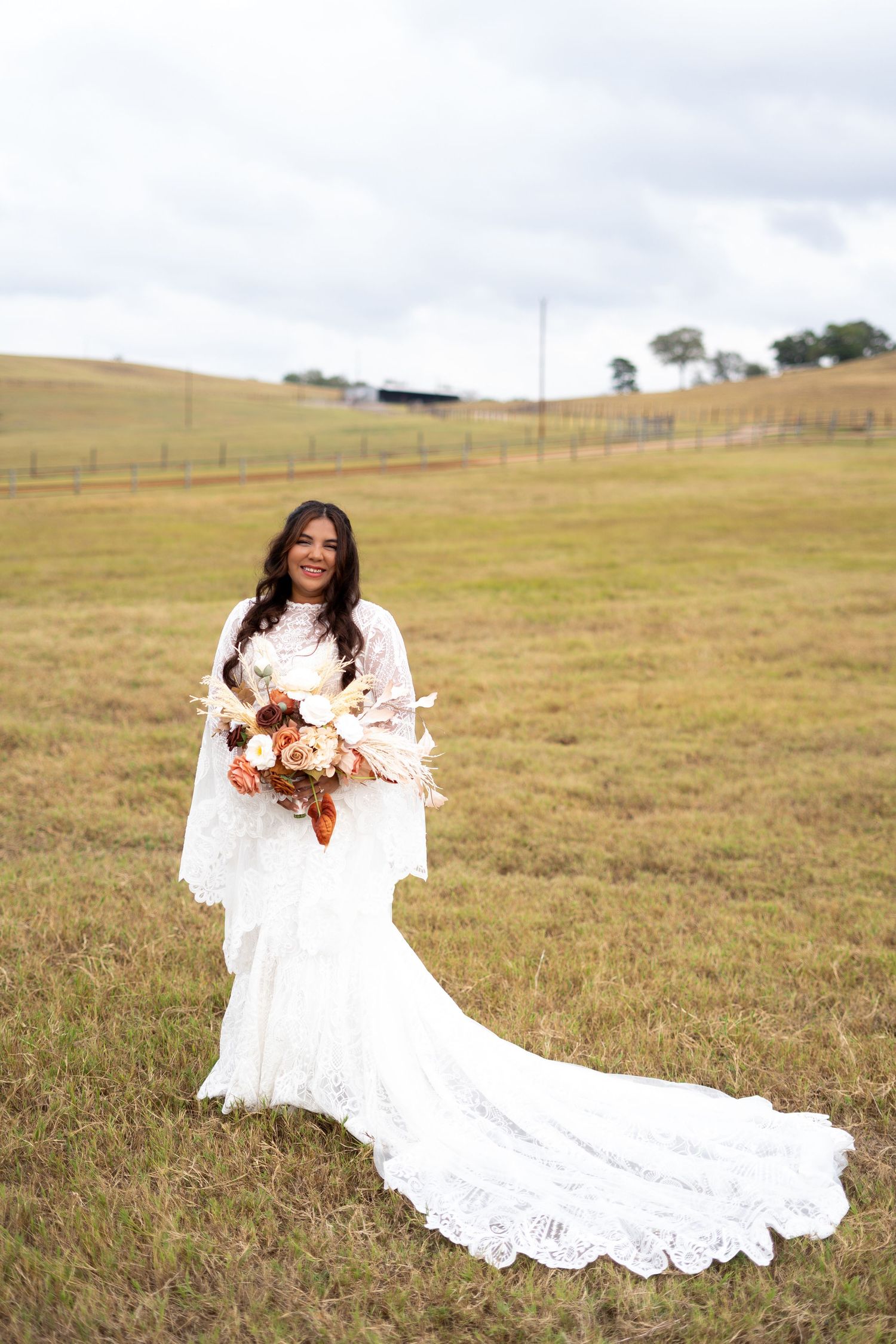 Bride in lace wedding dress posing in a golden field with flowing train.