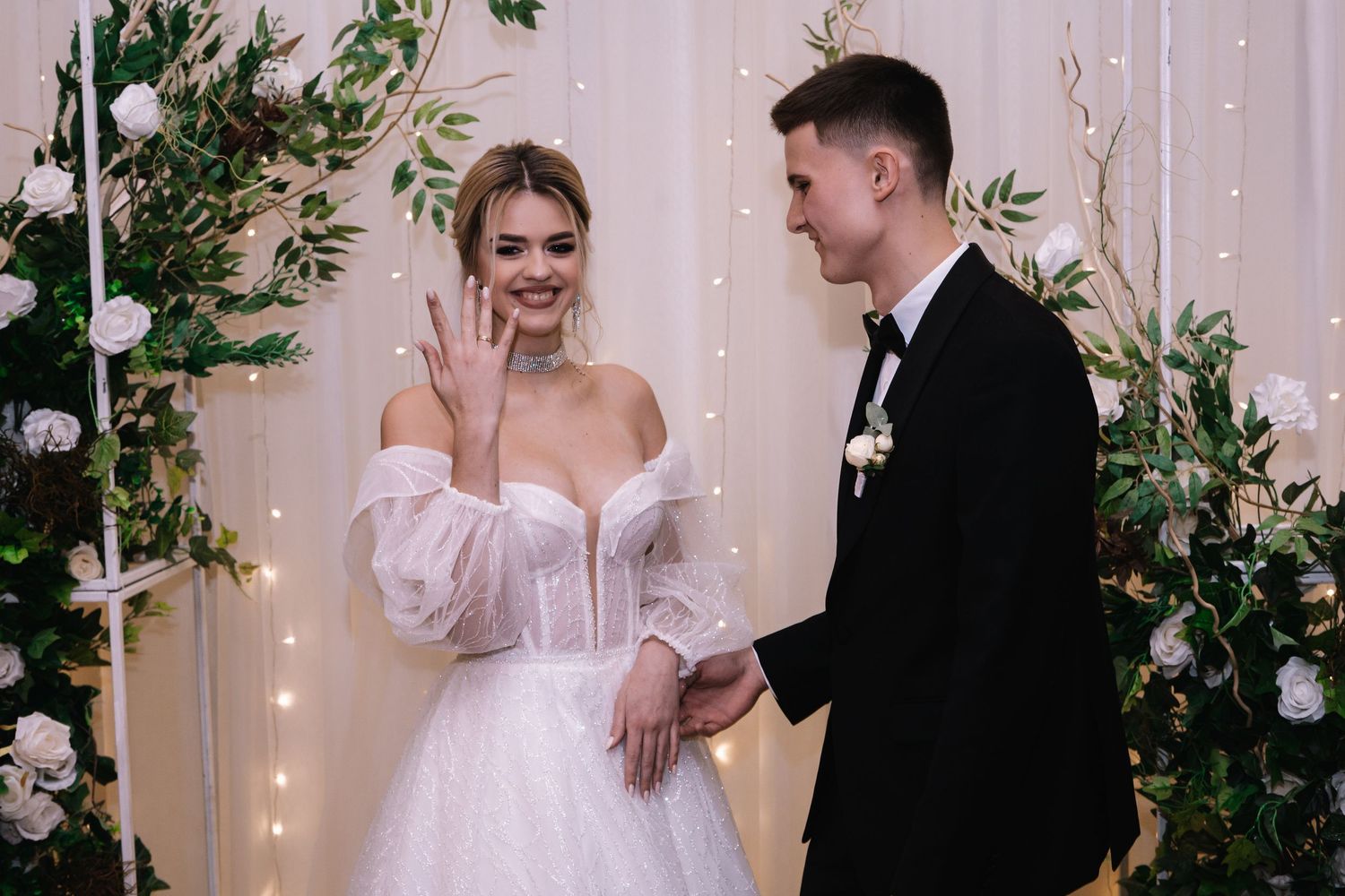 A couple shares a joyful moment during their wedding ceremony against a backdrop of twinkling lights and greenery.