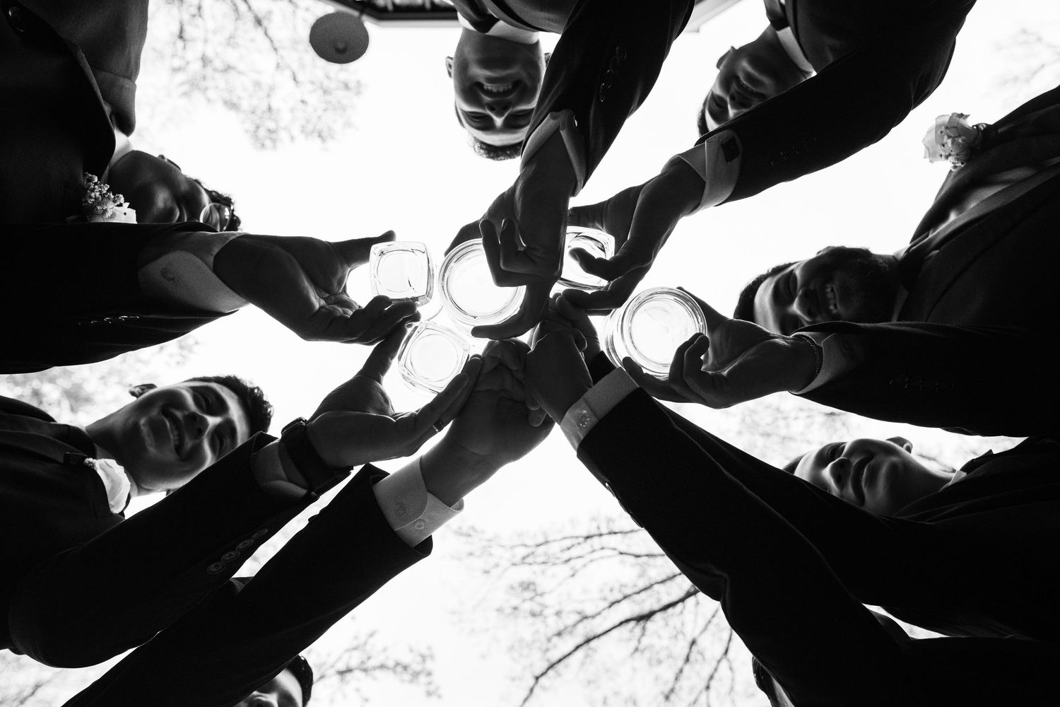 Low angle black and white shot of people forming a circle with their feet in athletic shoes against a bright sky.
