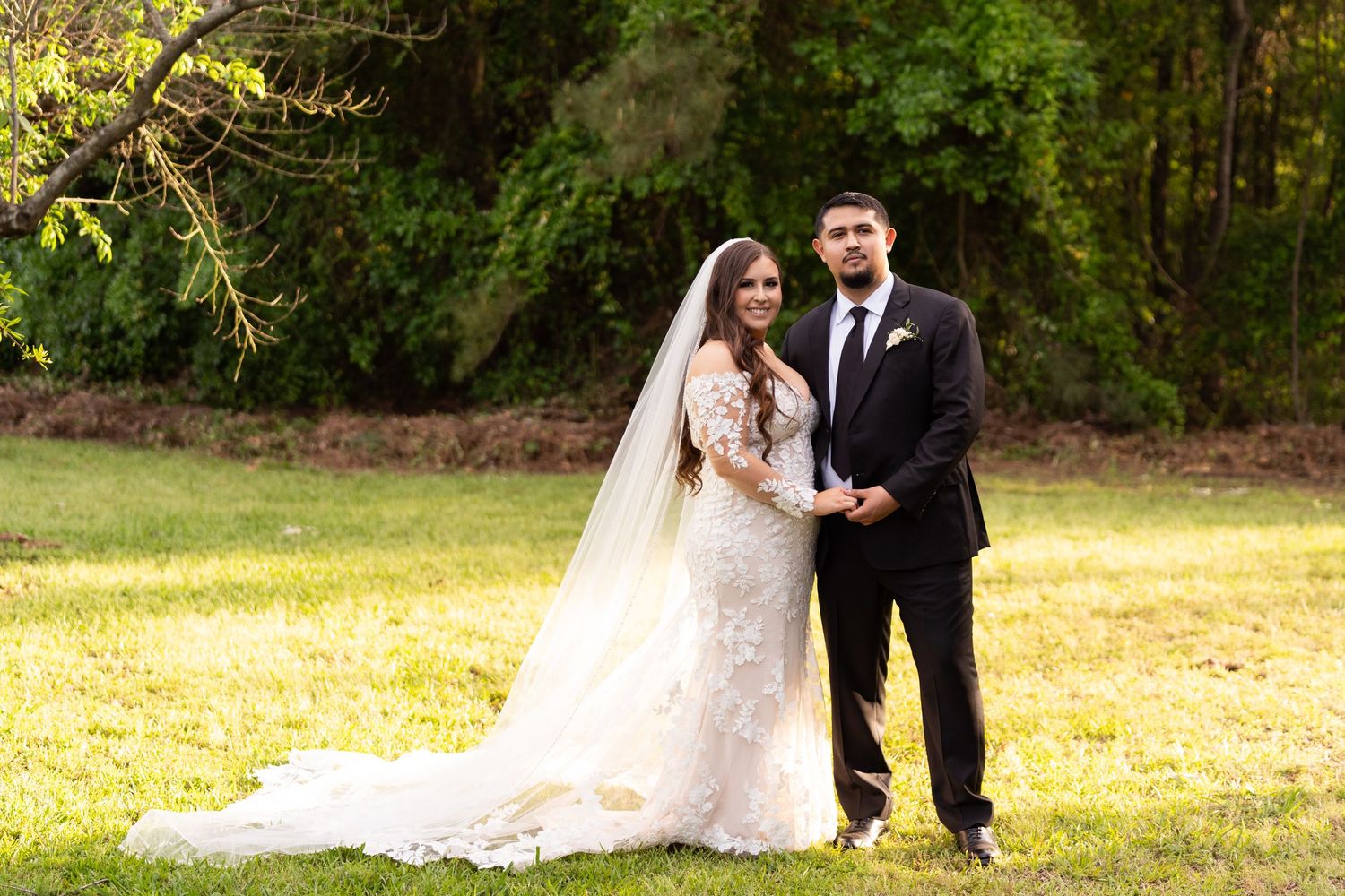 A couple in wedding attire walks through a lush green forest setting during their outdoor wedding photo session.