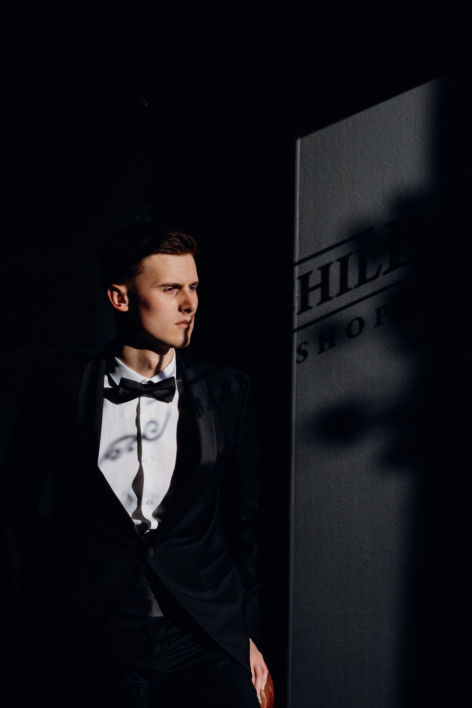 Dramatic black and white portrait of someone in a tuxedo and bowtie against a dark background with stark lighting.