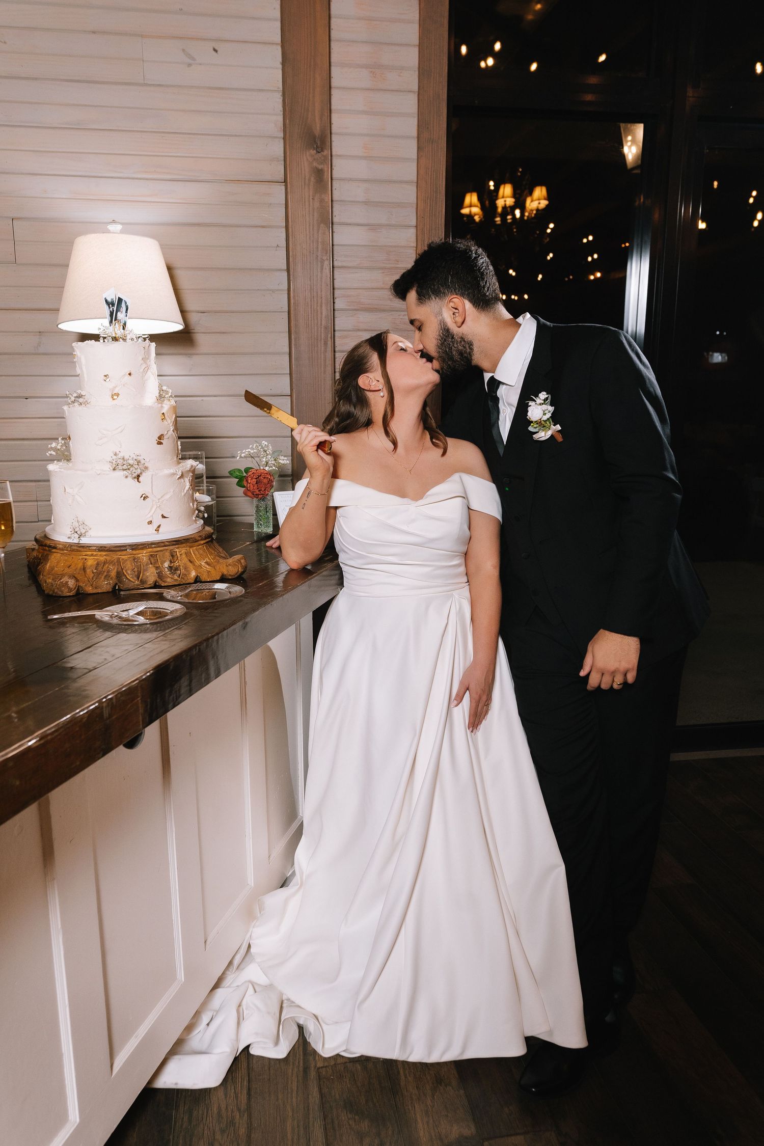 Wedding couple shares intimate moments near an elegant white tiered cake display.