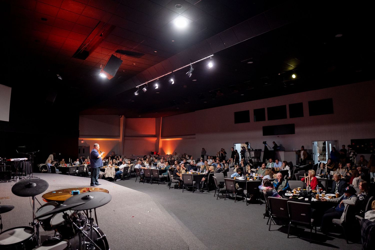 Wide shot of a darkened auditorium or conference space with spotlights and seated audience.