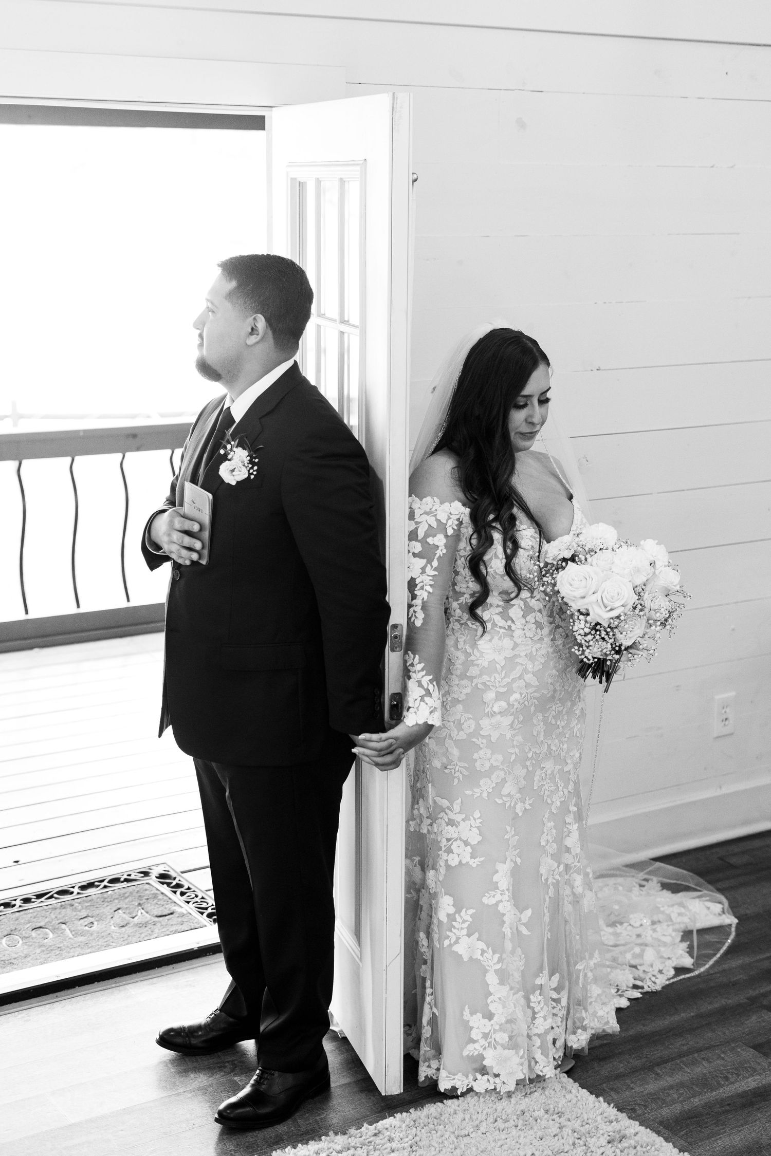 A bride and groom share a moment on opposite sides of a door before their wedding ceremony in black and white.