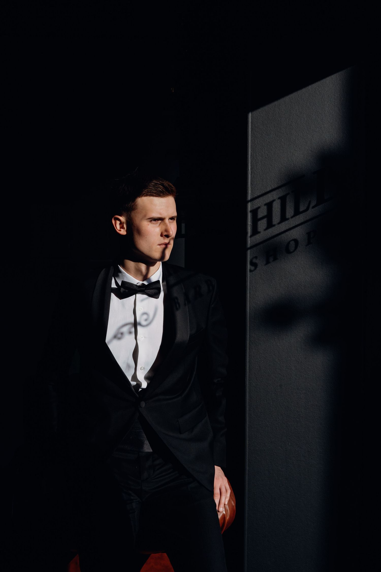 Dramatic black and white portrait of person in tuxedo and bow tie with moody shadows and lighting.