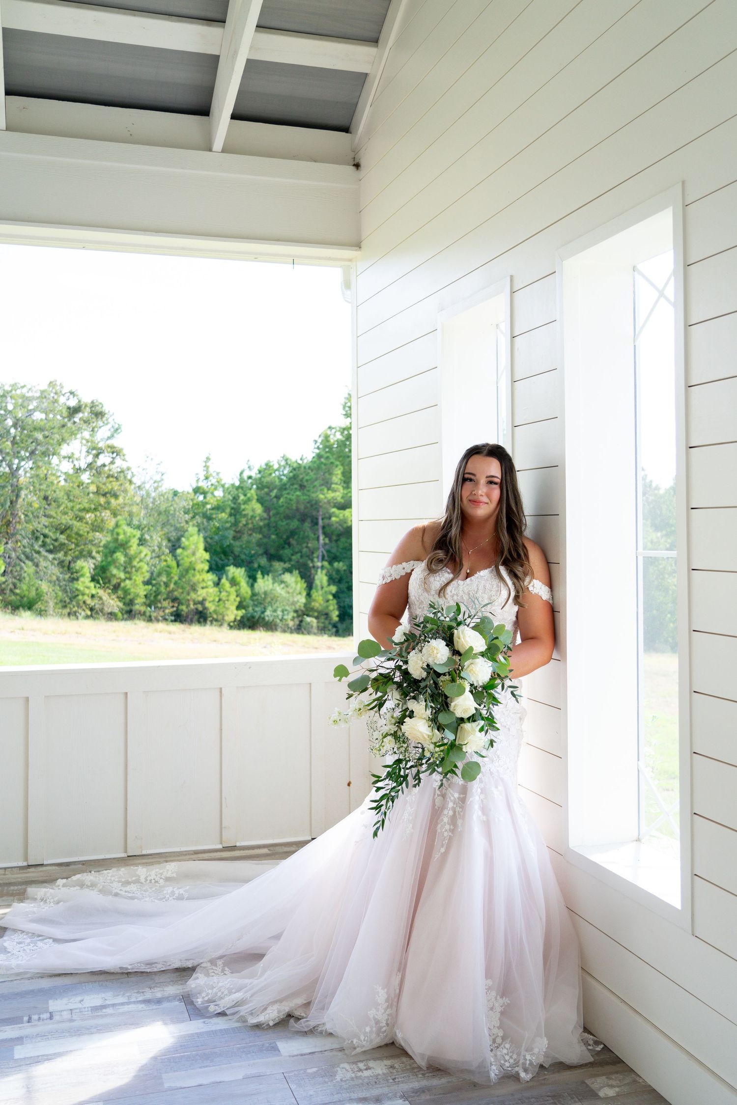 A cascading white and green bridal bouquet complements a flowing tulle wedding gown on a white porch.