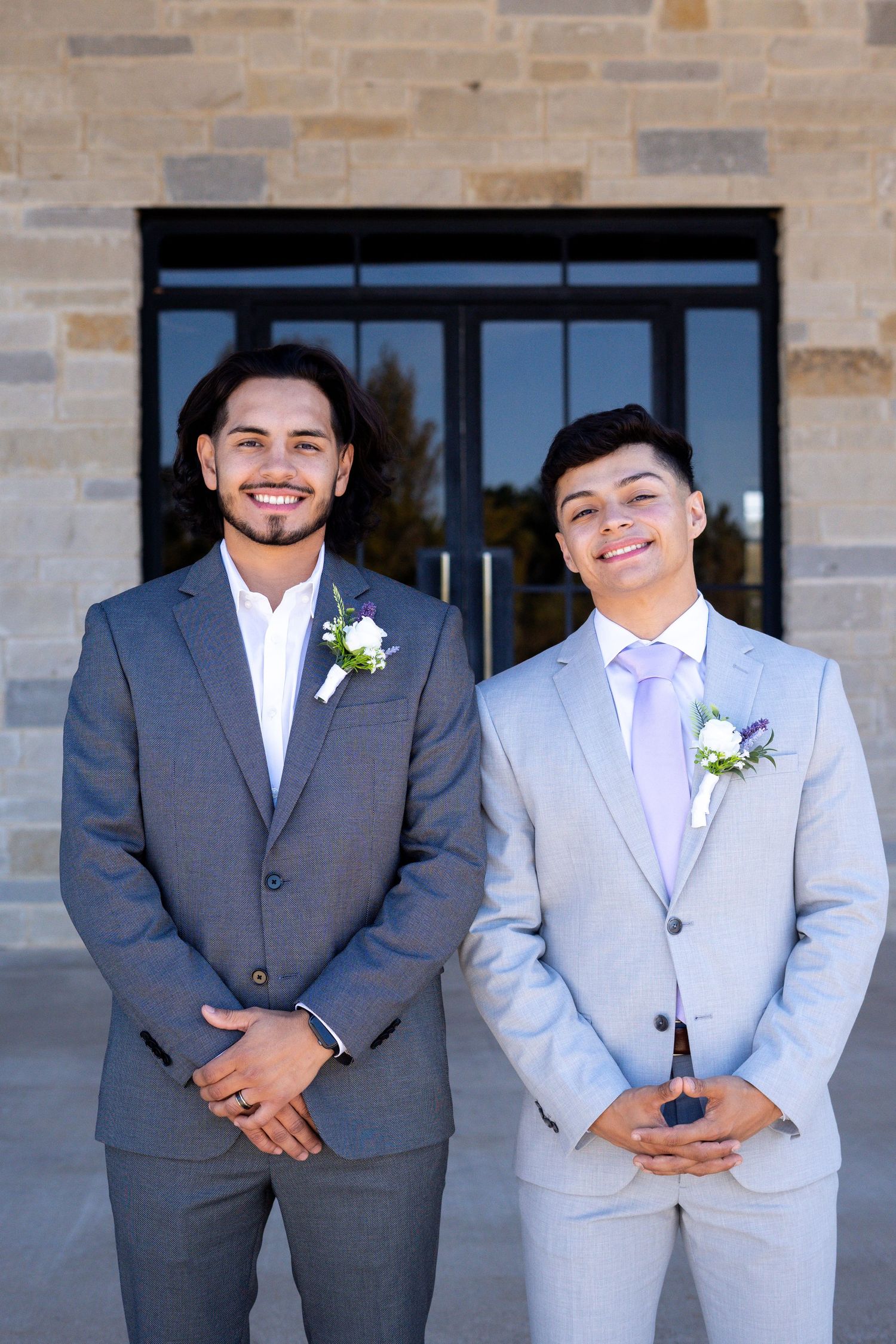 Wedding party members in contrasting gray suits and white boutonnieres pose against brick wall.