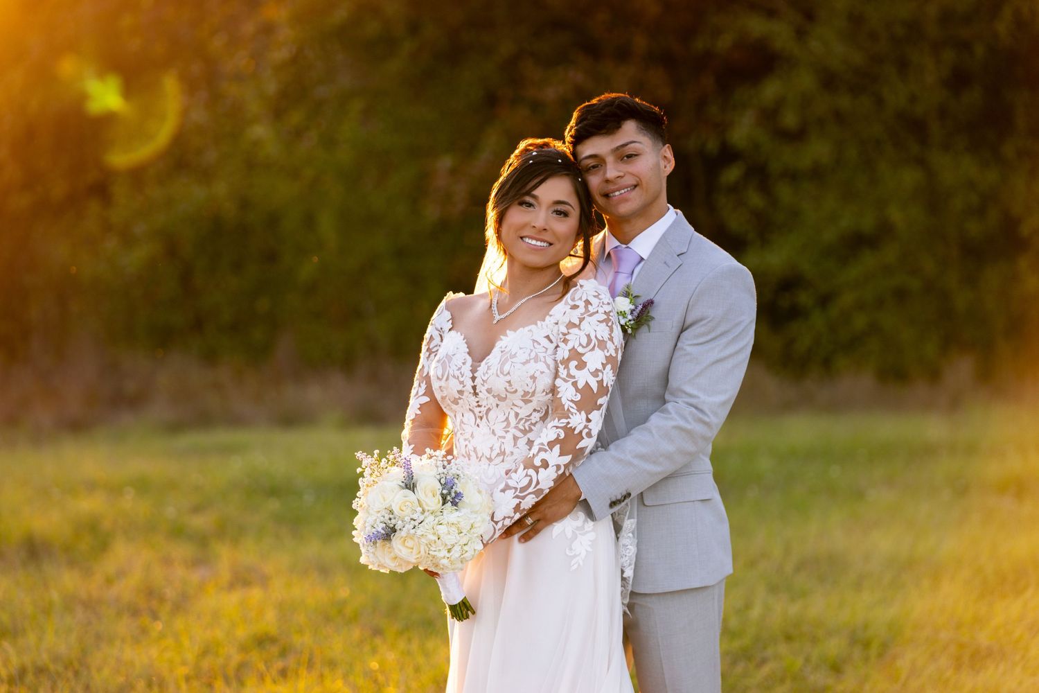 Newlyweds share intimate moment in warm autumn sunlight on grassy field.