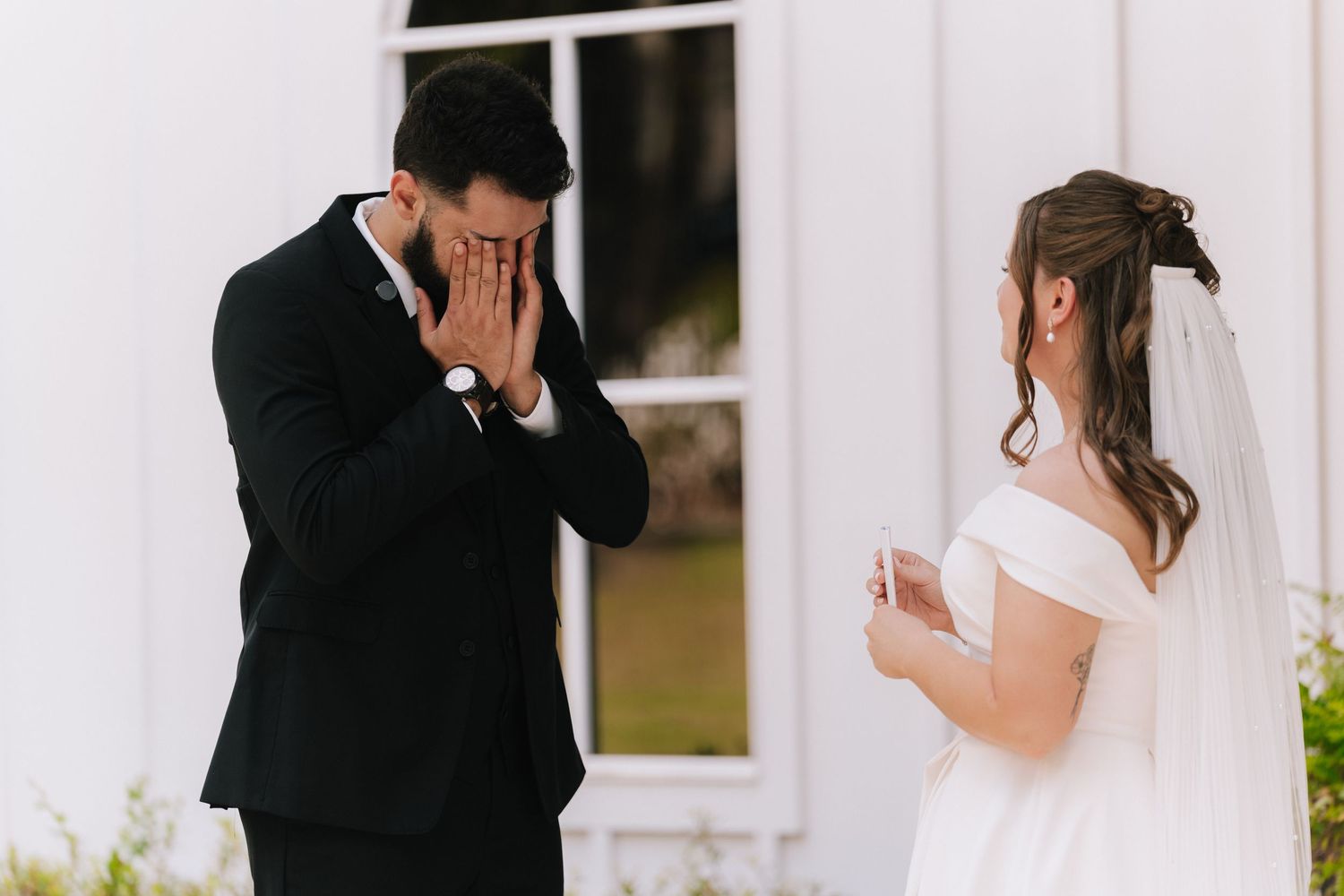 An emotional first look moment between a couple as the groom covers his face while the bride looks on.
