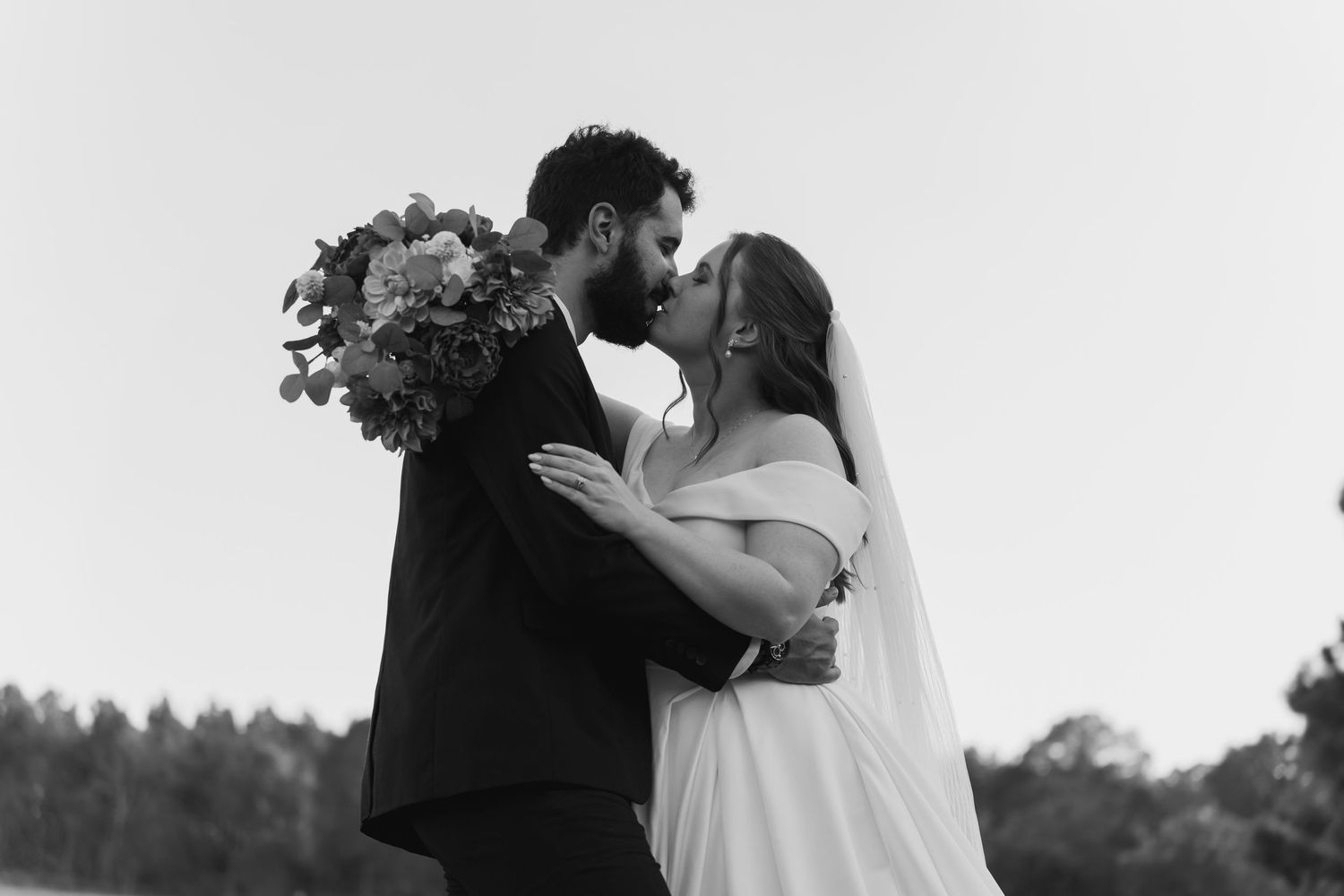 A romantic black and white photo of a couple embracing outdoors during their wedding.