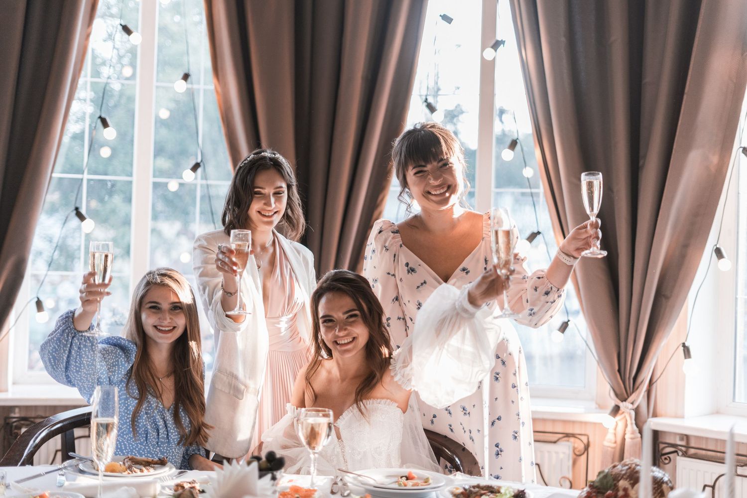 A group of friends in elegant attire raise champagne glasses for a celebratory toast at an indoor gathering.