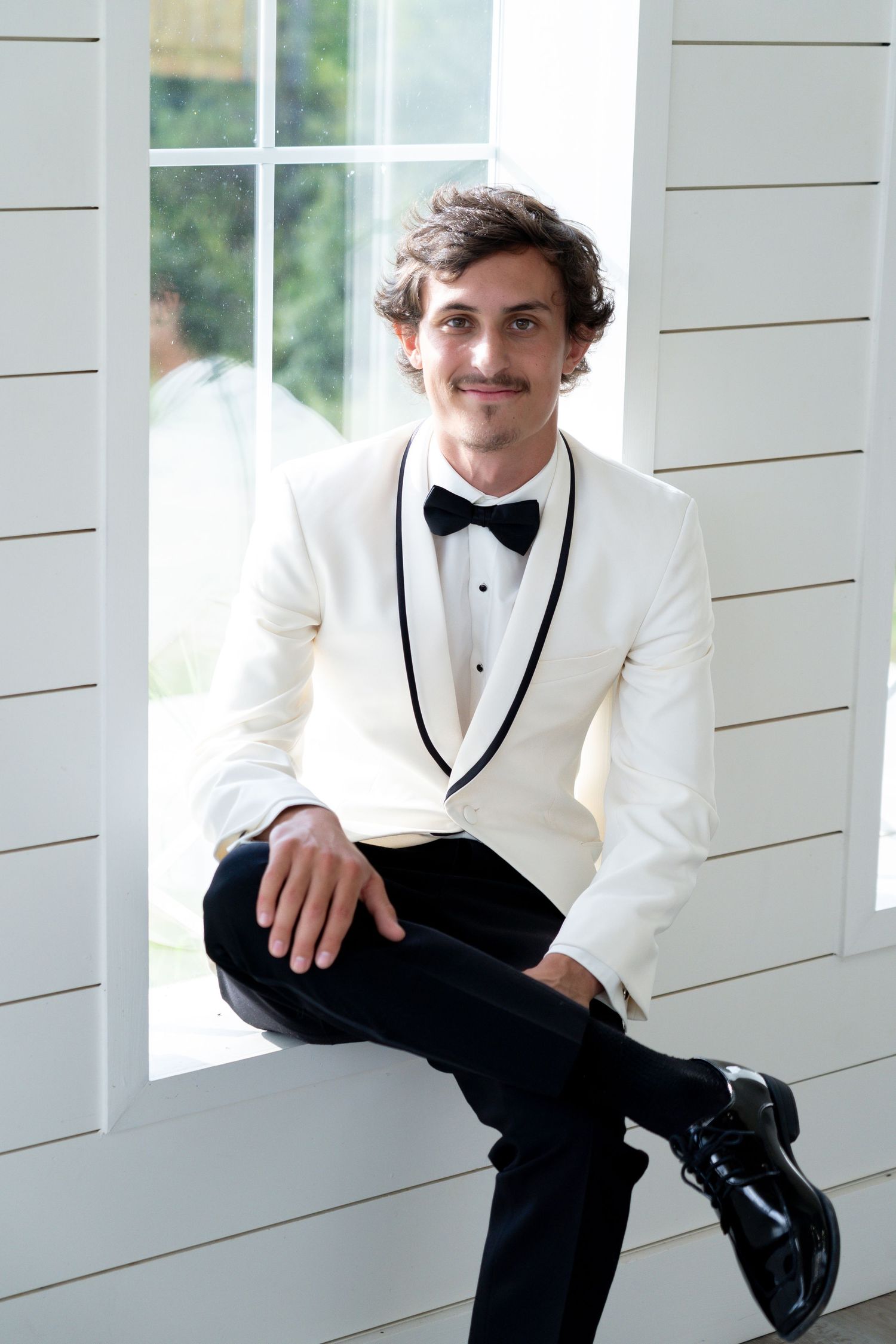 Elegant formal attire featuring a white dinner jacket with black lapels, bow tie, and black dress pants in a classic pose.