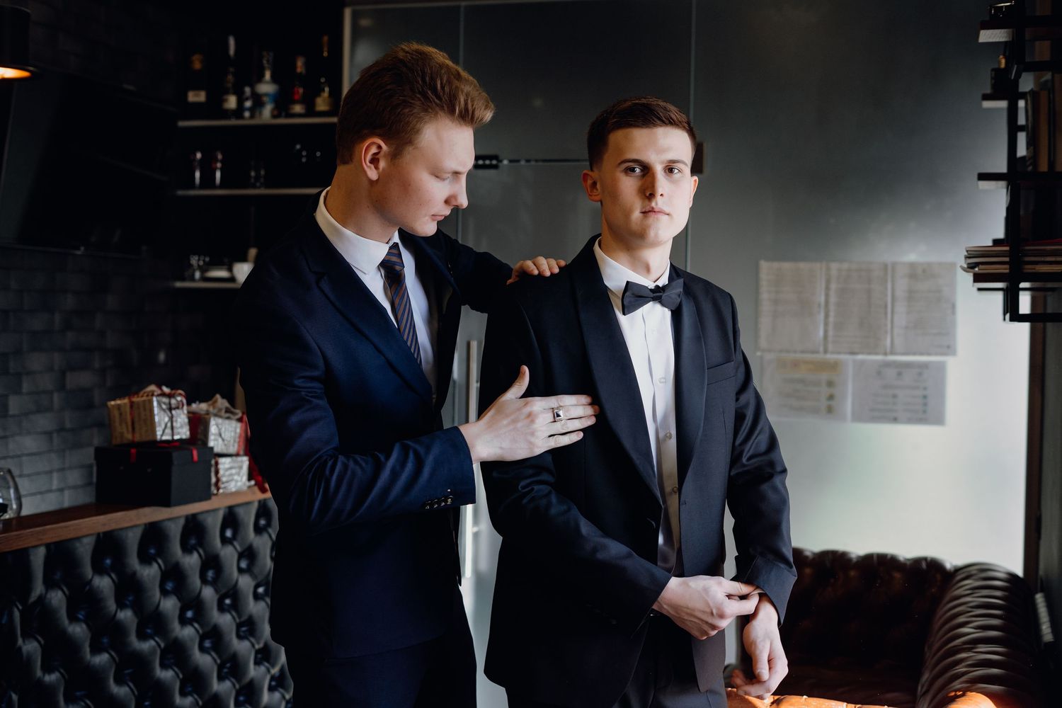 Two business professionals in dark suits sit at a table reviewing documents together in a modern office setting.