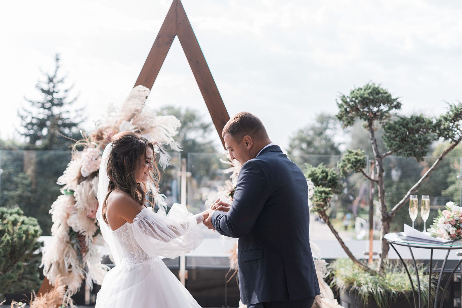 A couple shares a romantic moment during their wedding ceremony surrounded by floral arrangements and outdoor scenery.