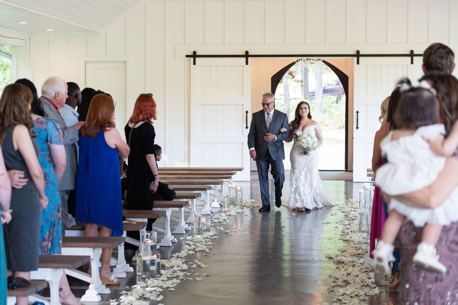 A couple walks down a covered porch aisle lined with white chairs during an intimate wedding ceremony.