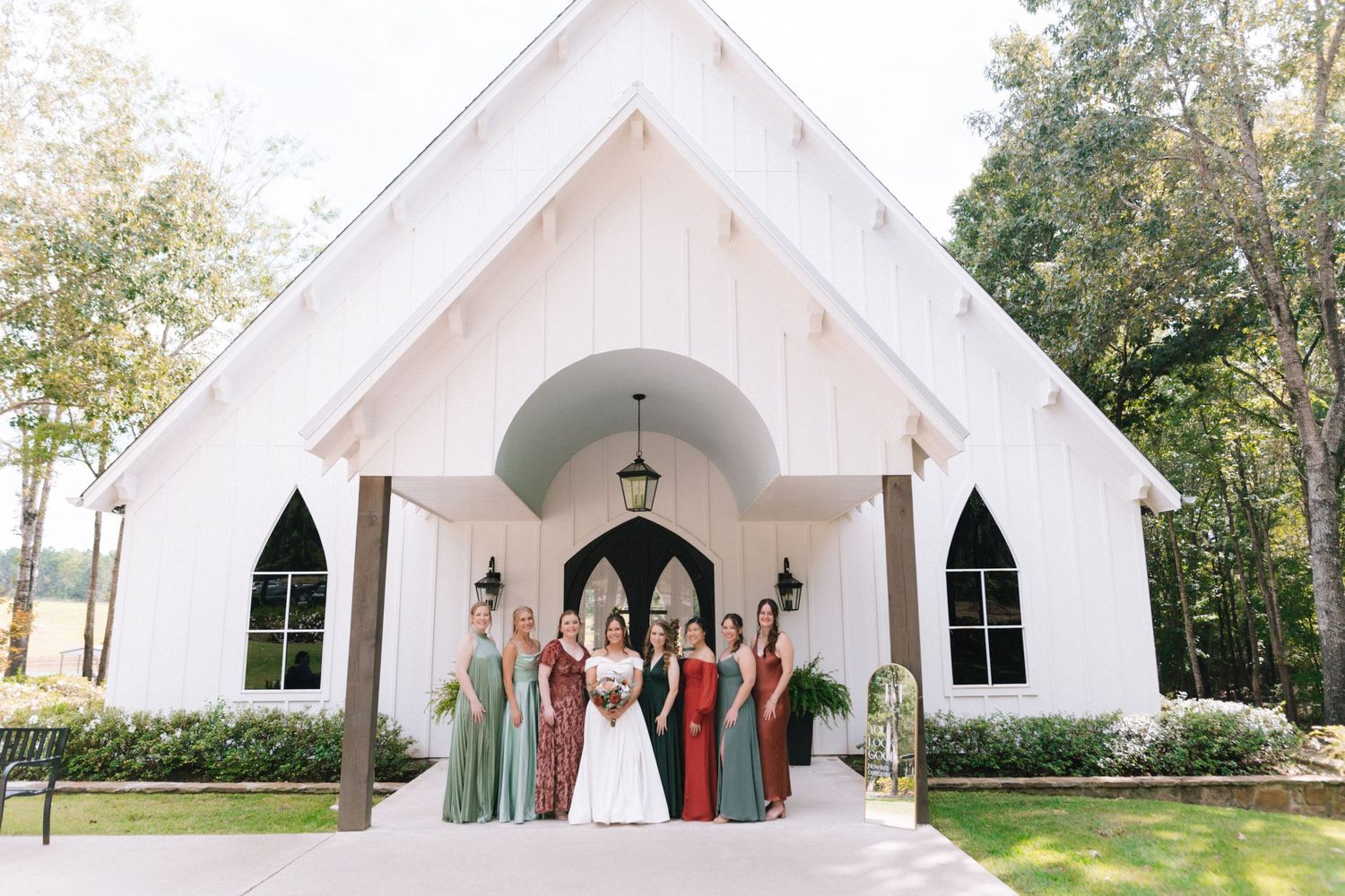 A panoramic view of a white chapel wedding venue with gothic windows and multiple entrances surrounded by trees.