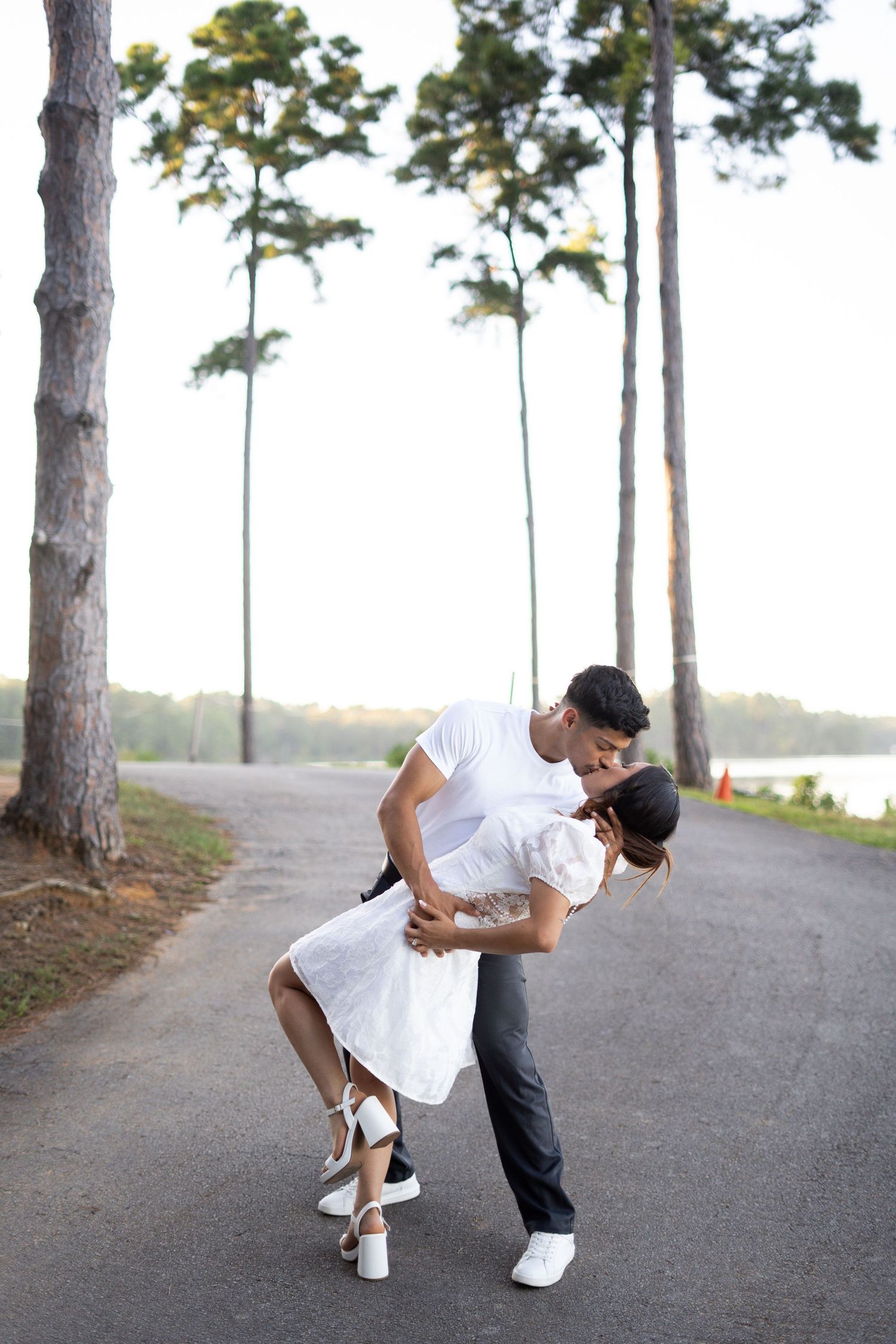 Couple performs romantic dance dip on outdoor path surrounded by pine trees.