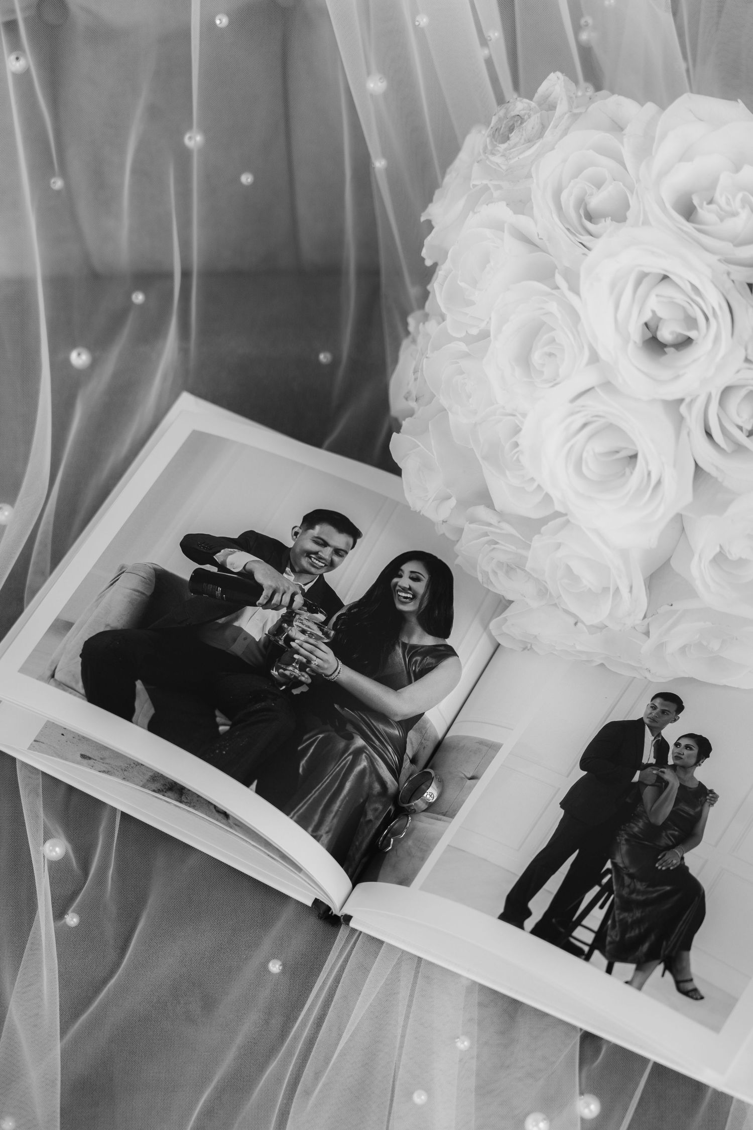 Black and white photographs of a couple displayed against a white tulle fabric background with decorative roses.