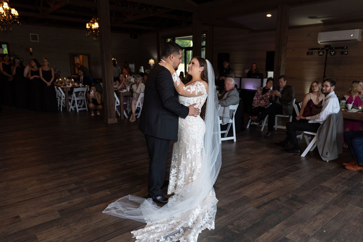 Wedding guests dance and celebrate on a dark wooden dance floor during an evening reception celebration.