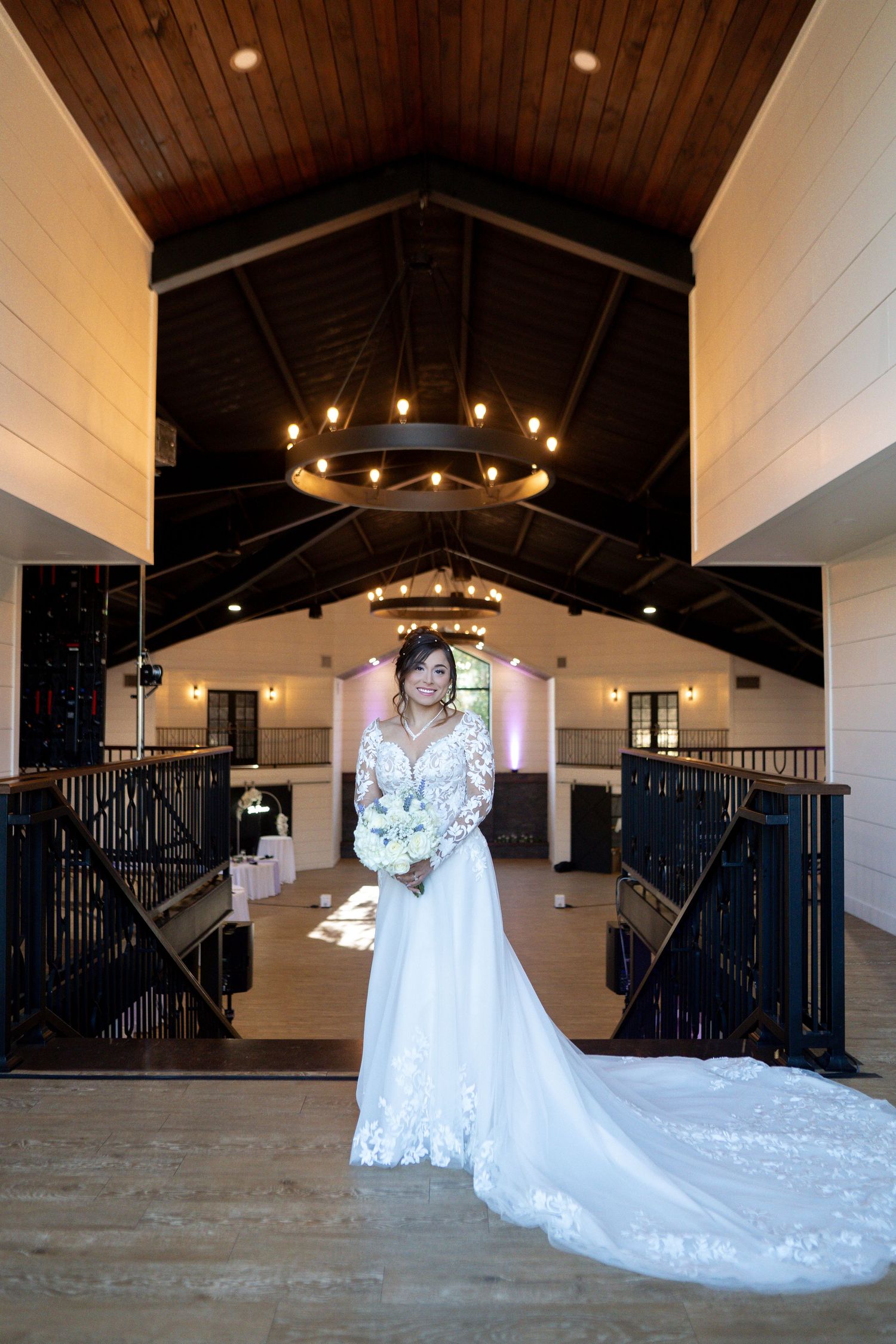 A stunning wedding dress with a long train displayed in an elegant venue with wooden beams and chandeliers.
