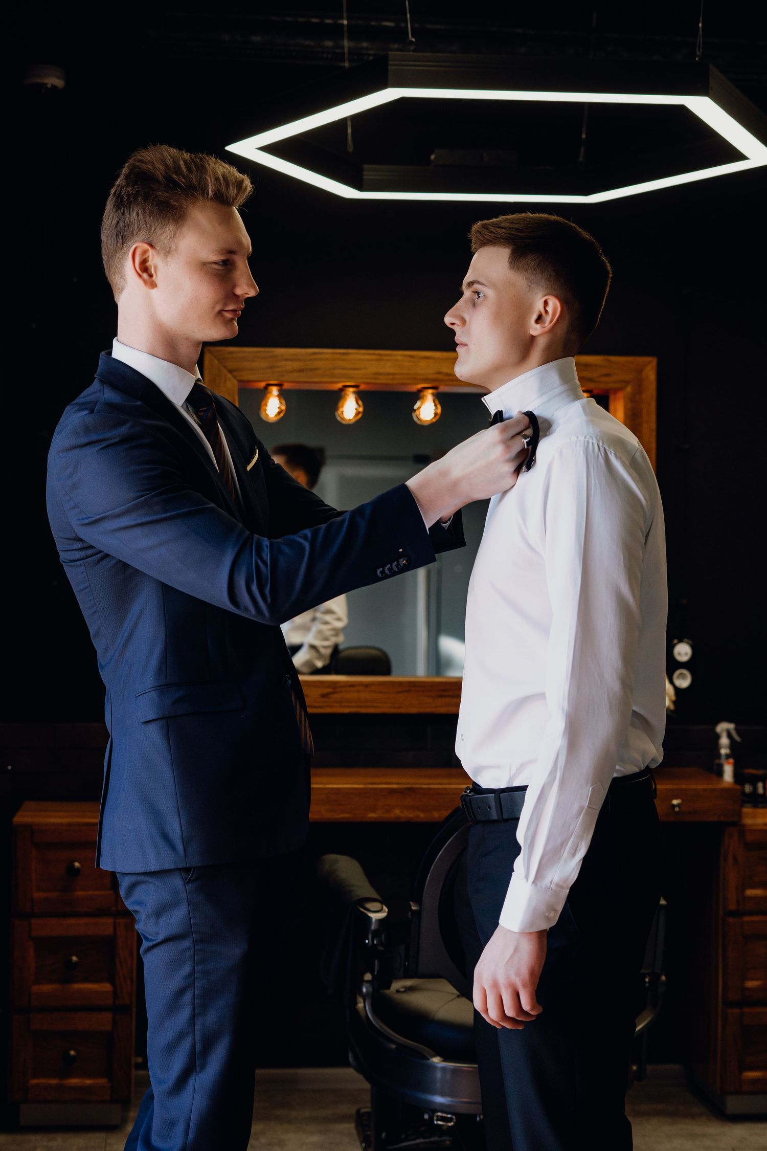 Two people in formal attire help each other adjust their clothing and accessories before an event.