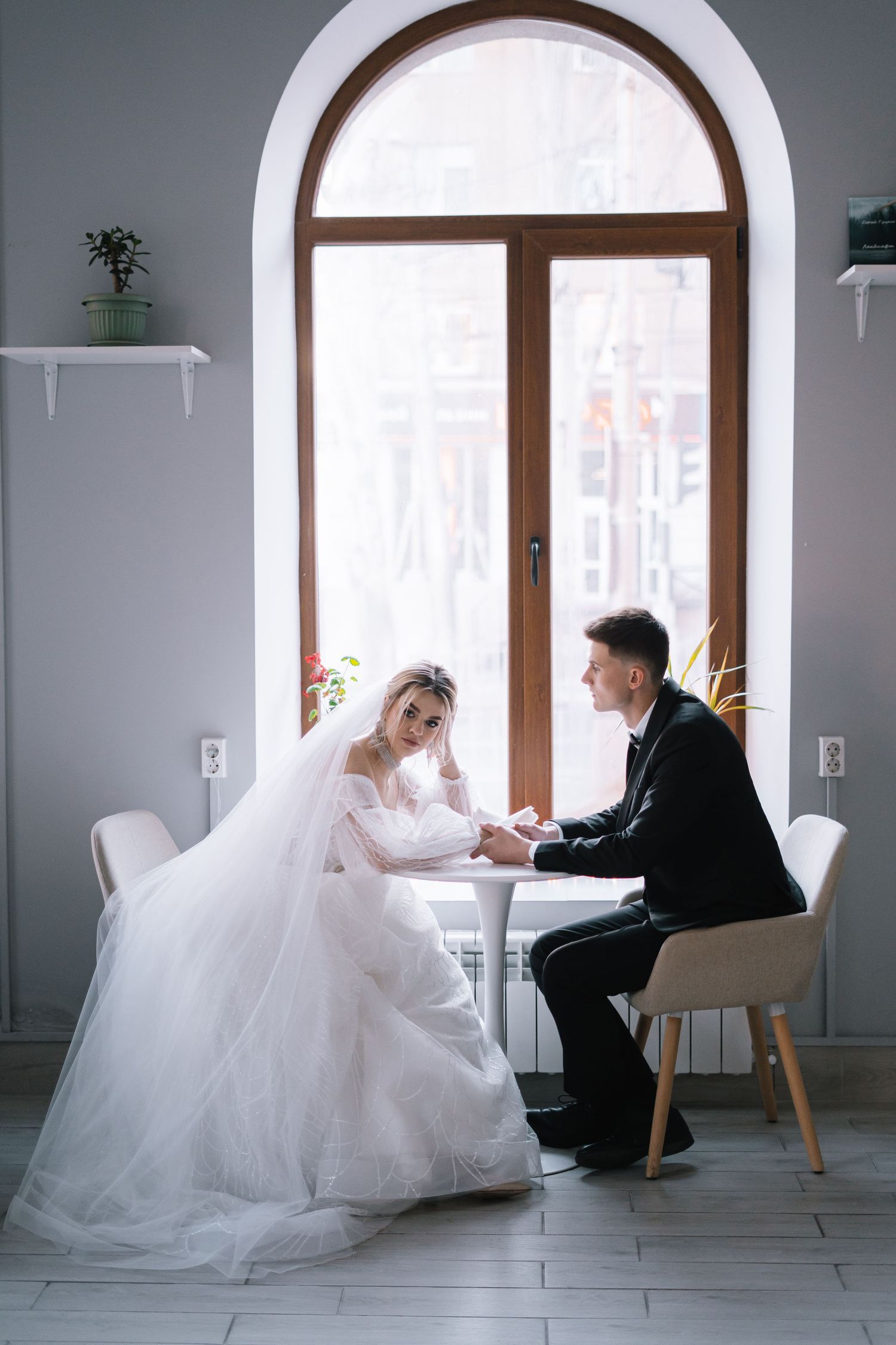 A series of romantic wedding photos showing a couple in formal attire sitting at a table by an arched window.