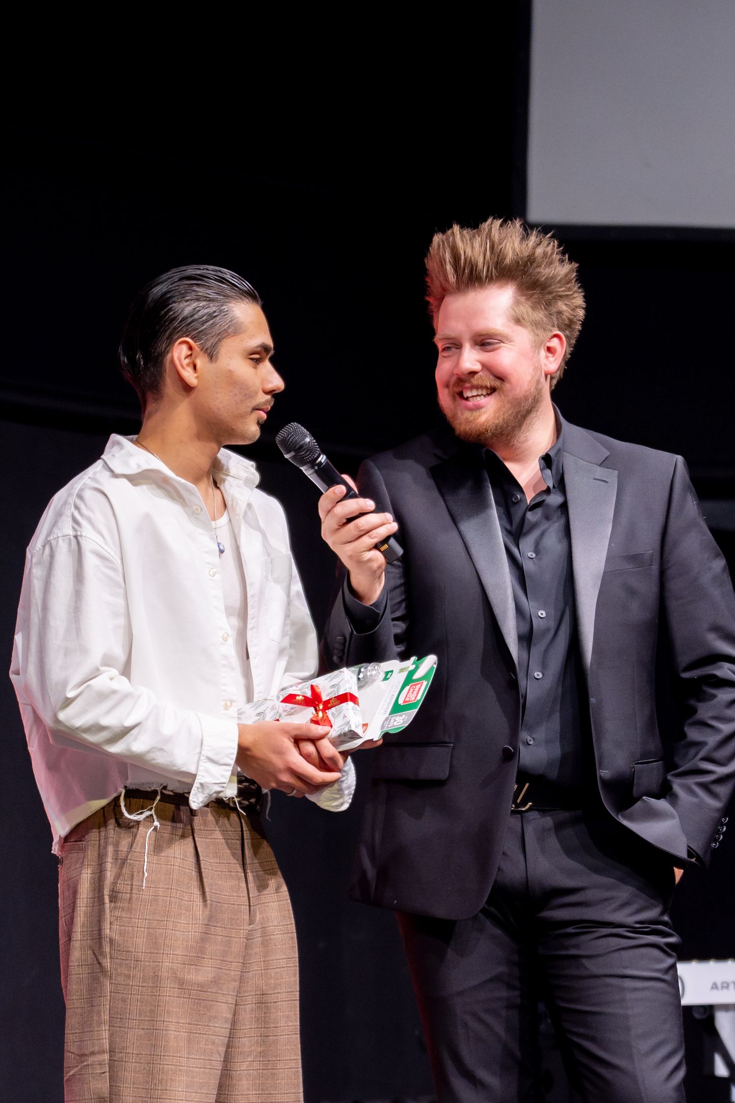 Two performers share a lighthearted moment on stage during a presentation.