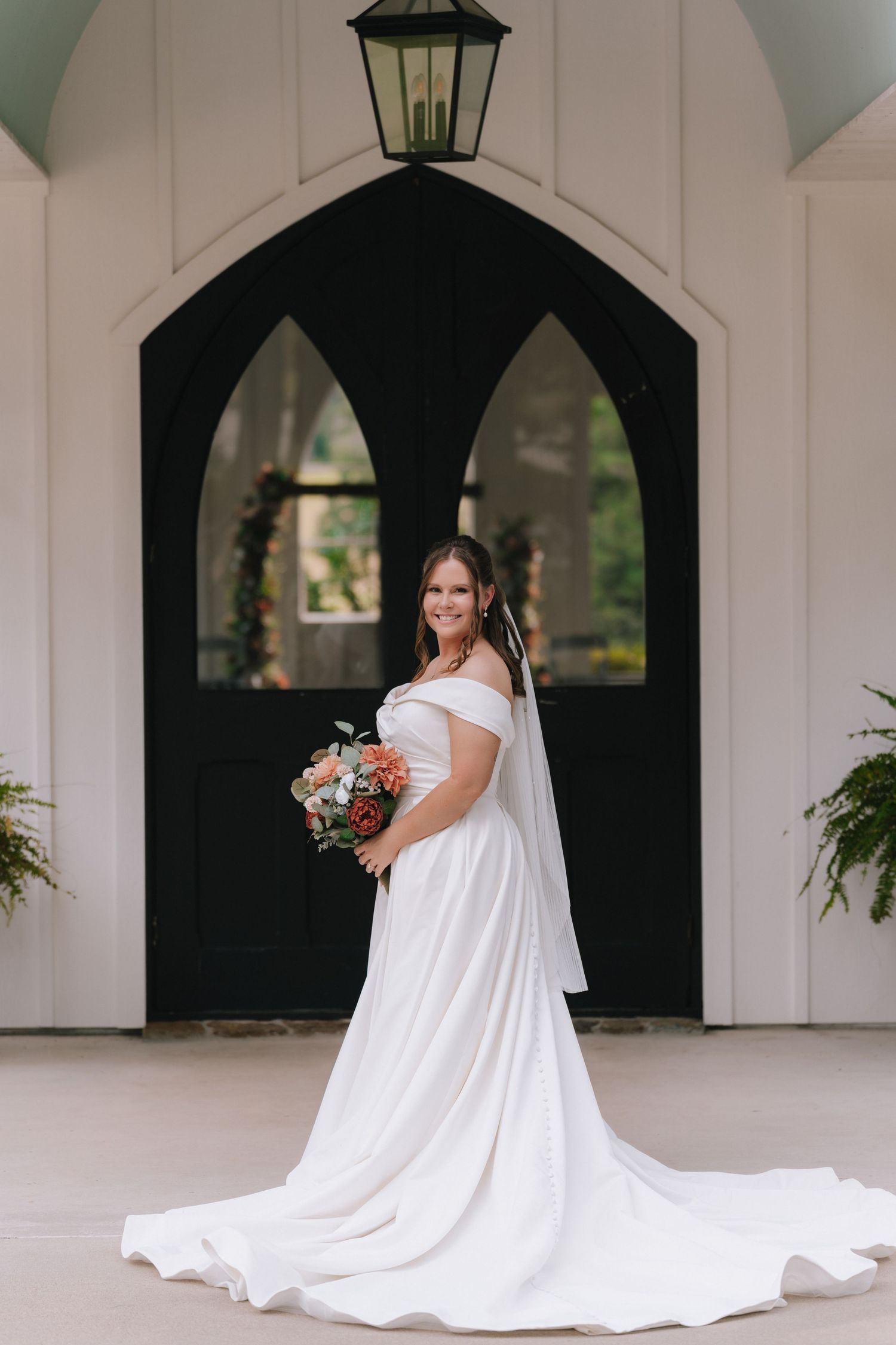 Bridal portrait in front of white chapel walls with gothic arched windows.