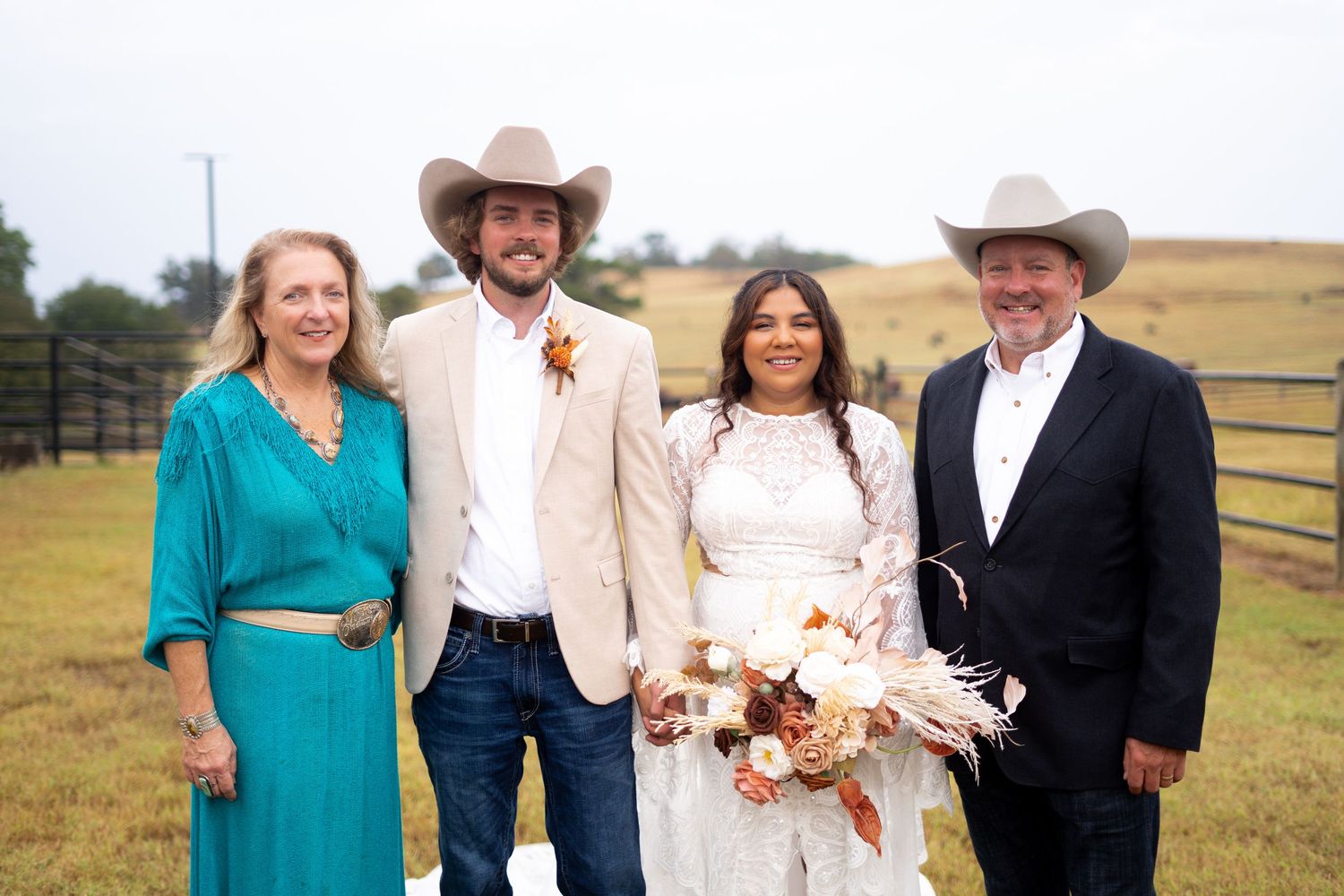 Wedding party in western attire posing outdoors in rustic ranch setting.