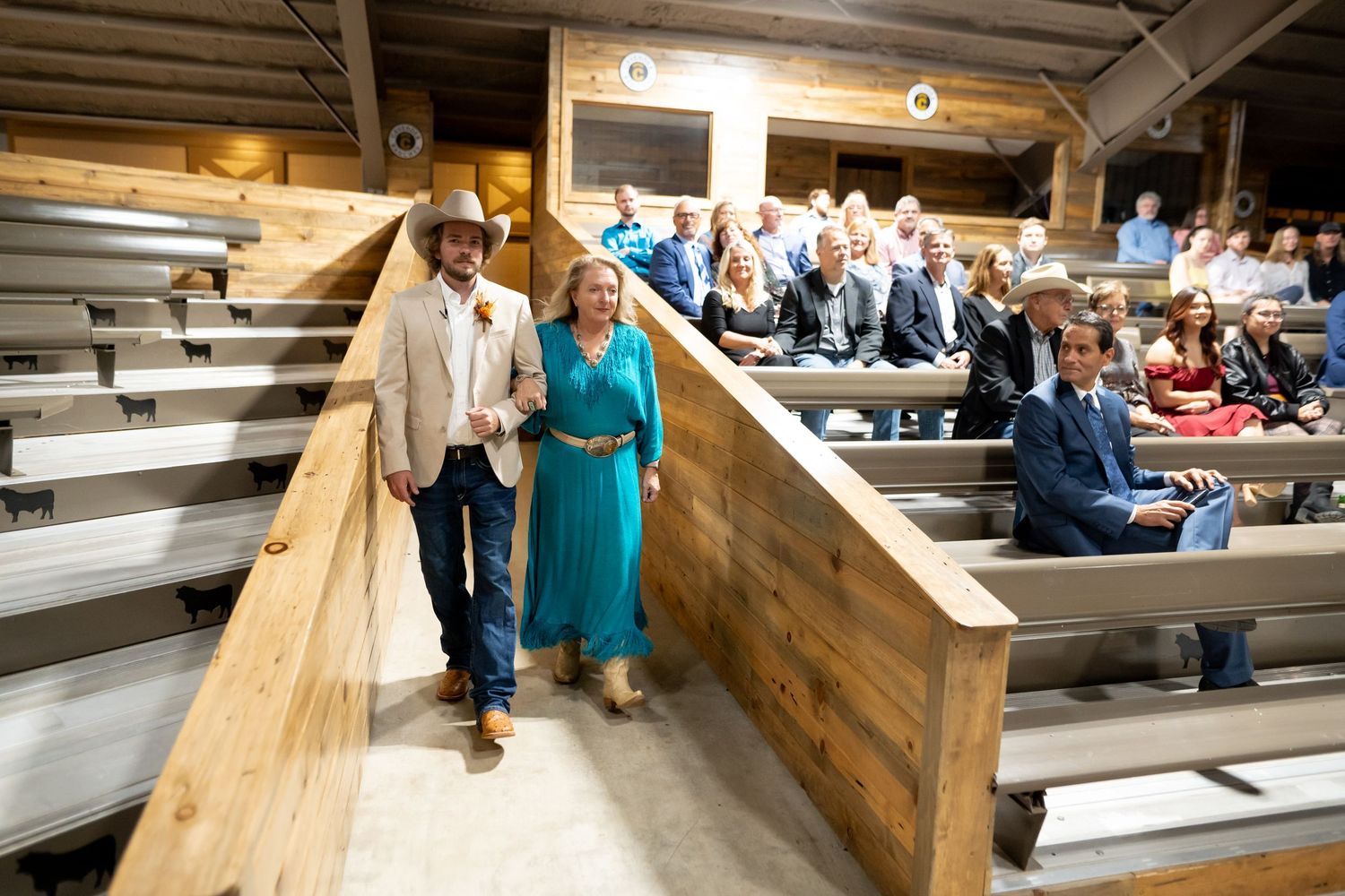 Wedding guests walk down wooden bleacher-style seating at an indoor venue.