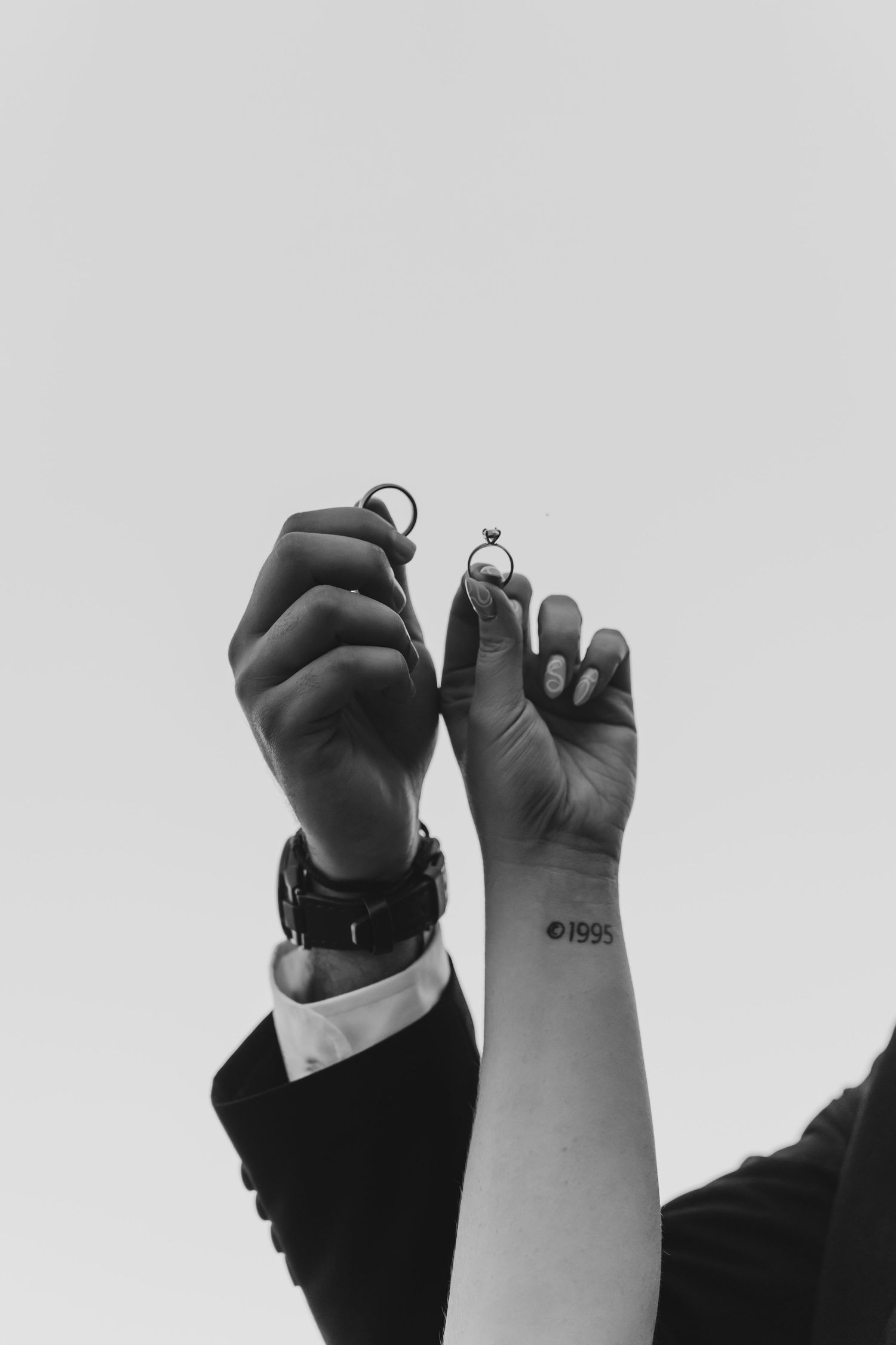 Black and white close-up of raised fists showing wedding rings.