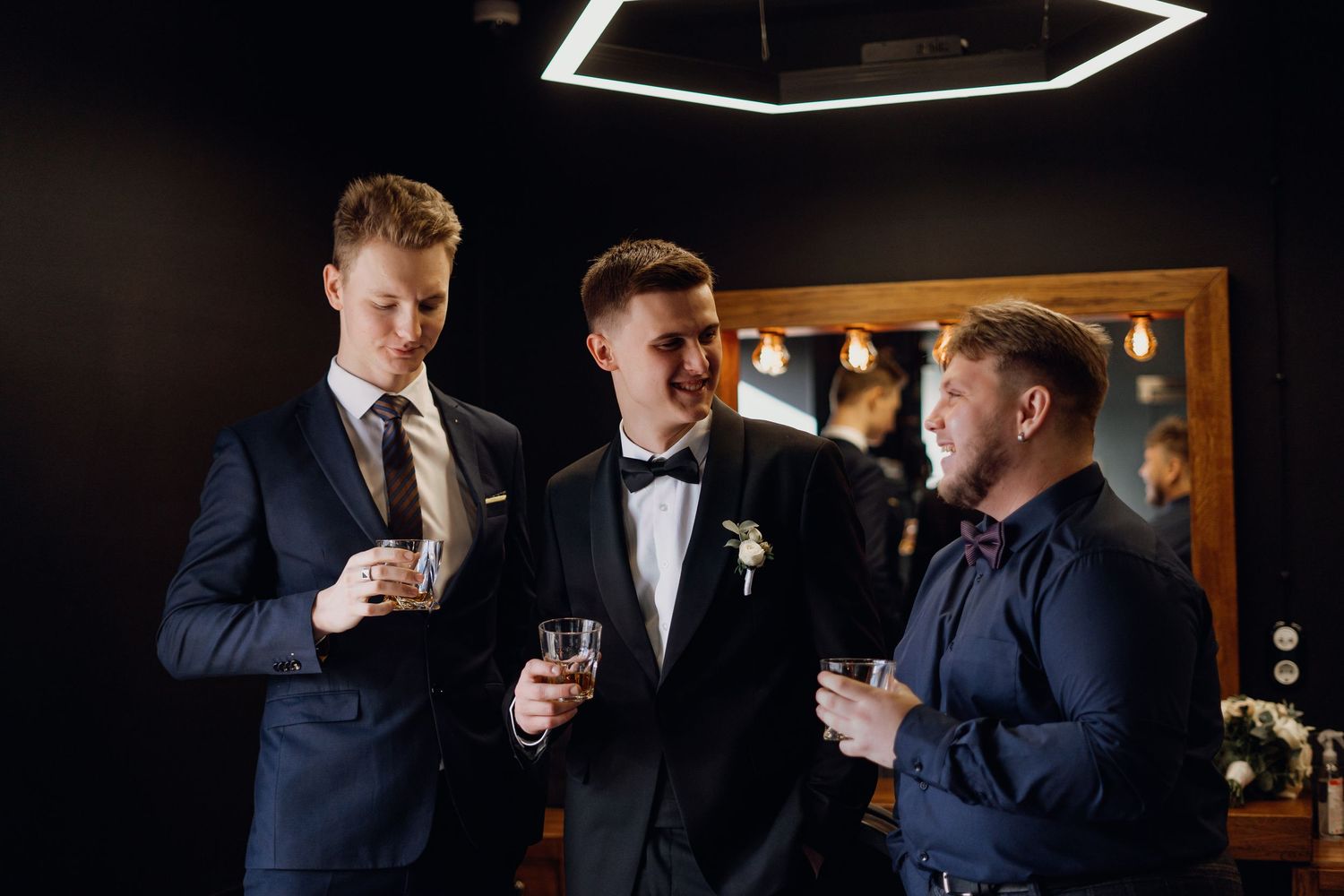 Groomsmen in navy and black suits gather in a dark bar setting with ambient lighting.
