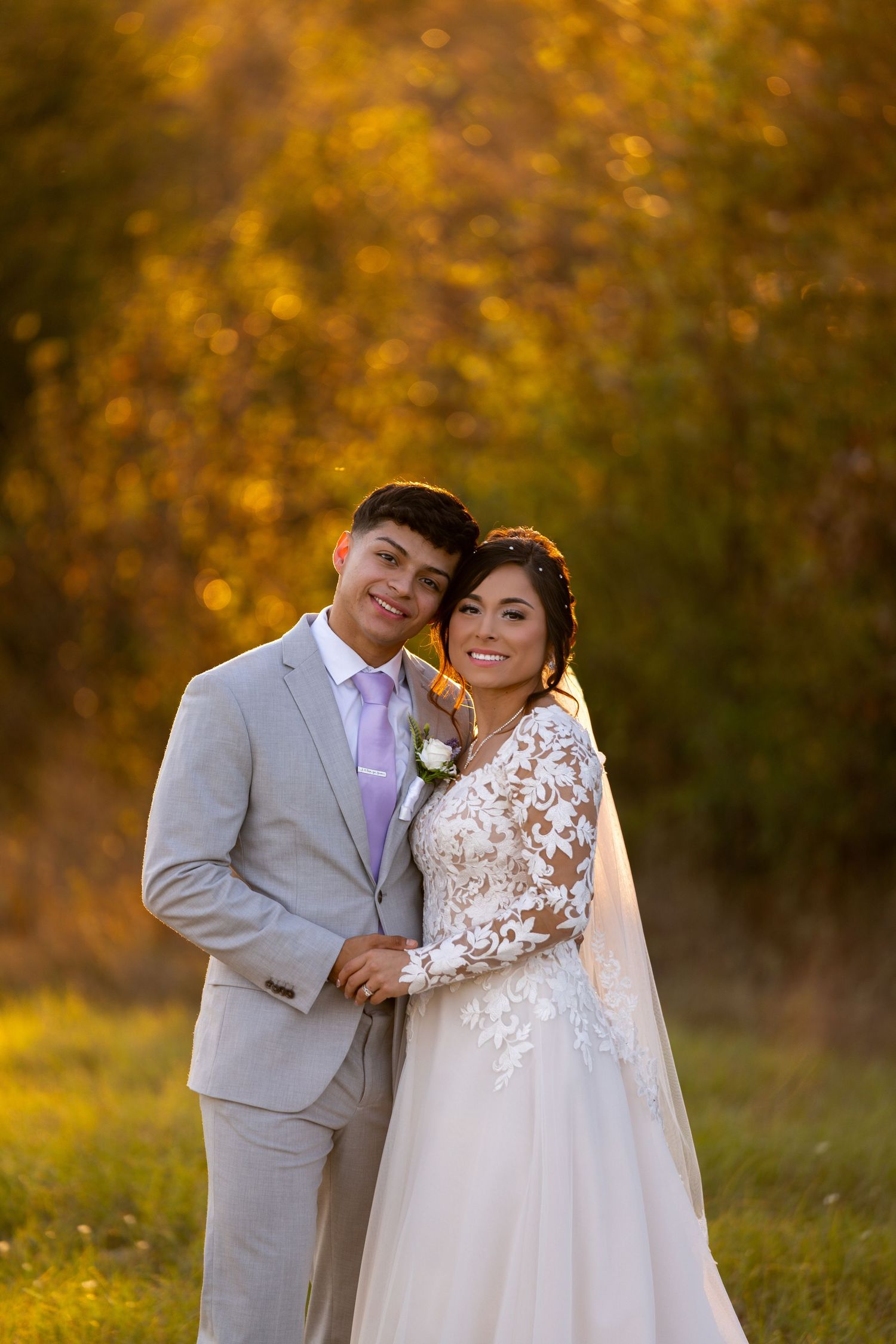 Newlyweds pose together in a field during golden hour with autumn colors in background.