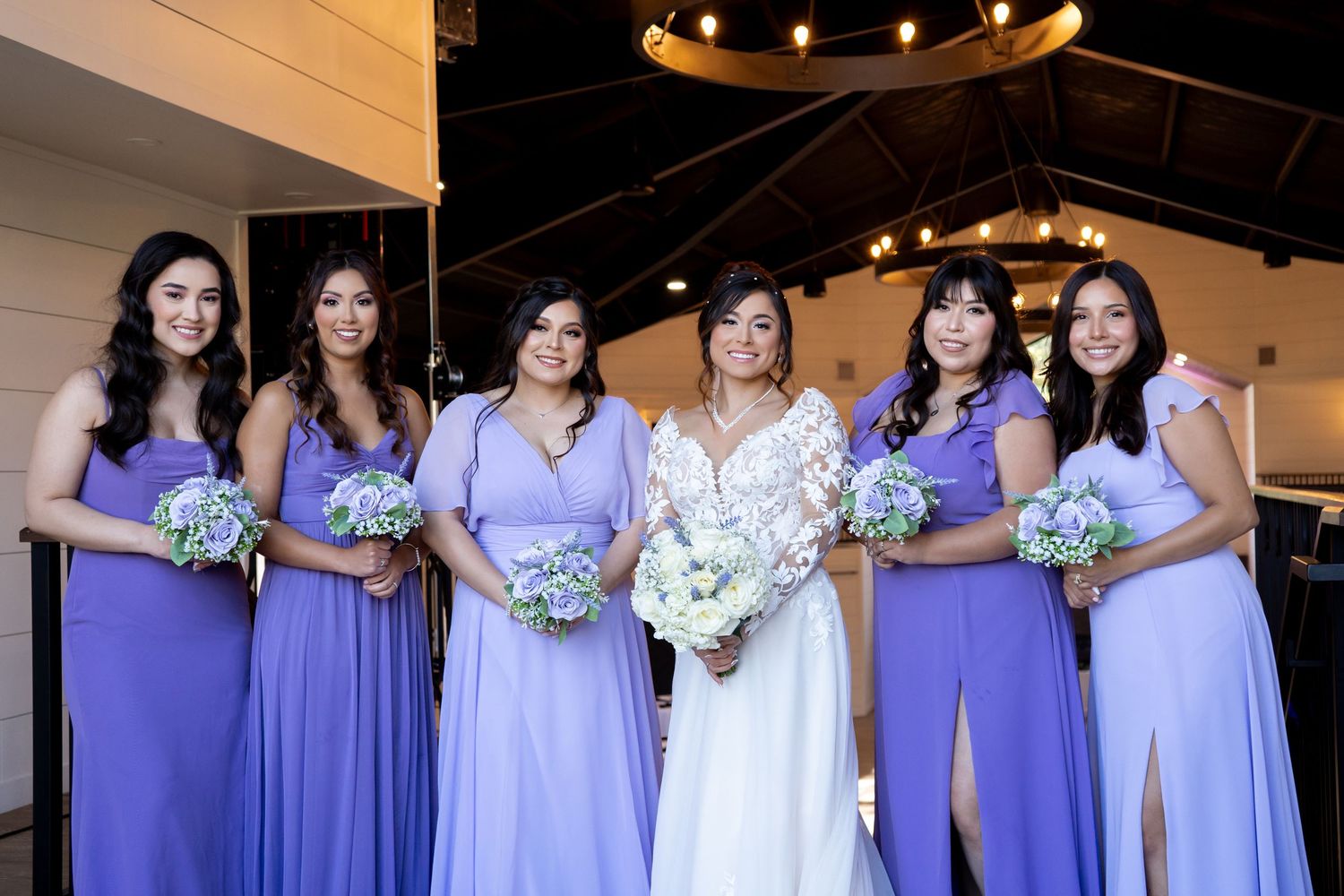Bridesmaids in lavender dresses pose together holding white floral bouquets.