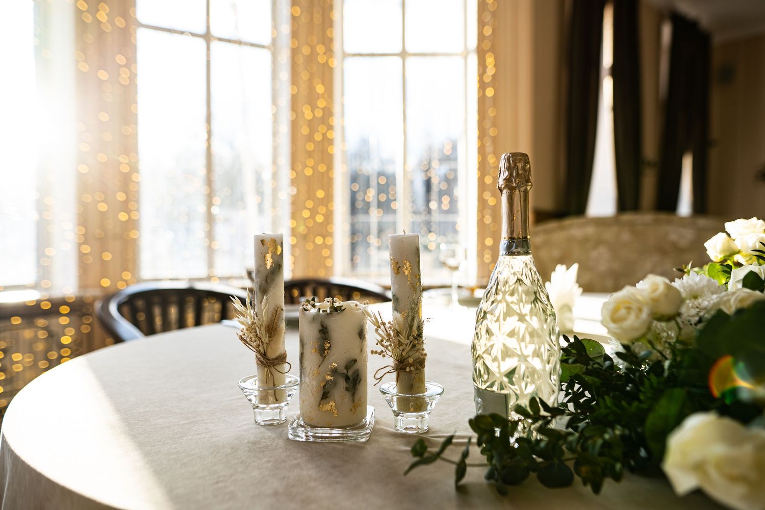 Elegant table setting with sunlit window, champagne bottle, crystal candlesticks and white floral arrangements.
