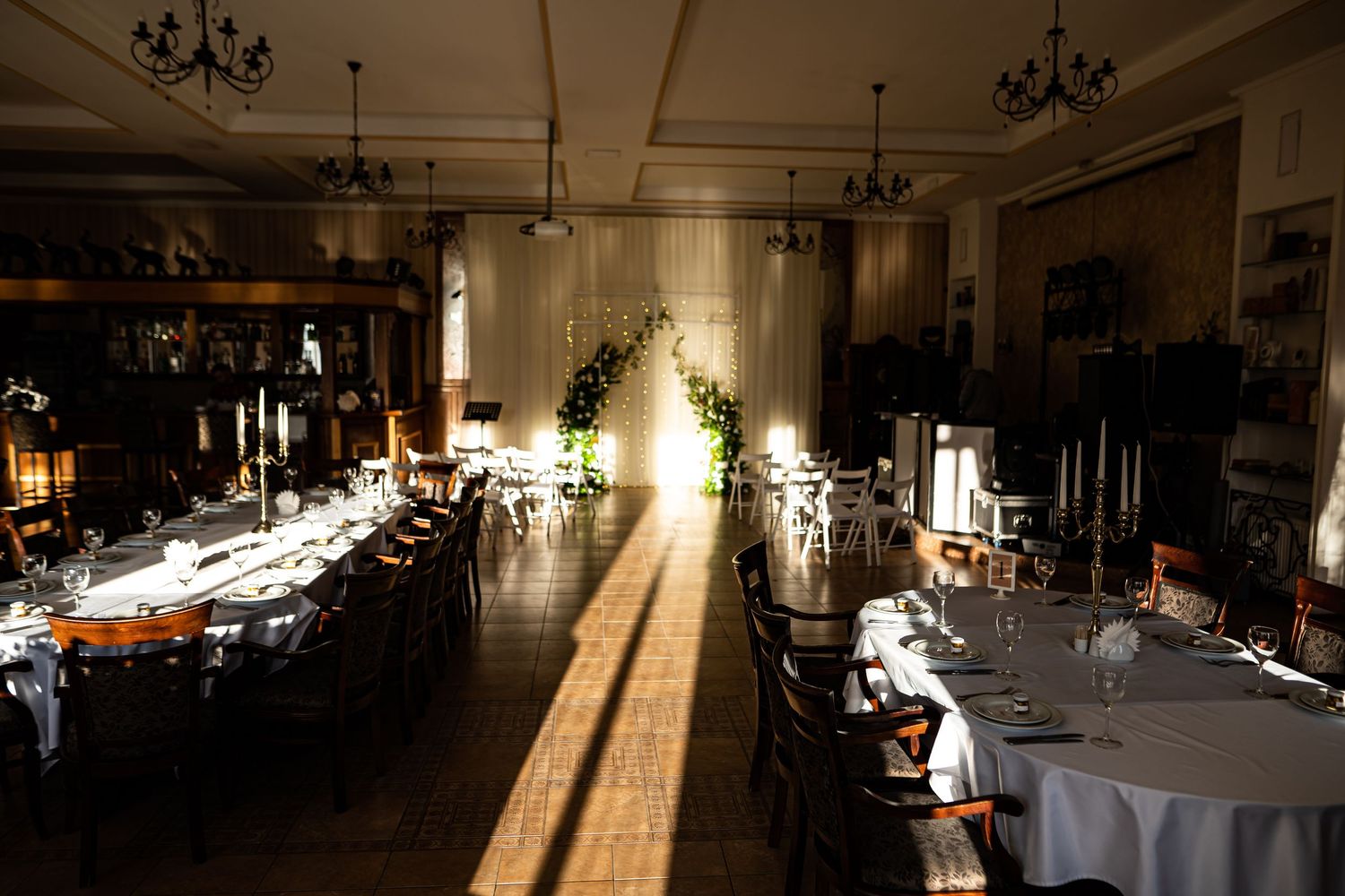 Elegant wedding reception venue with chandeliers and round tables set for dinner in warm lighting.