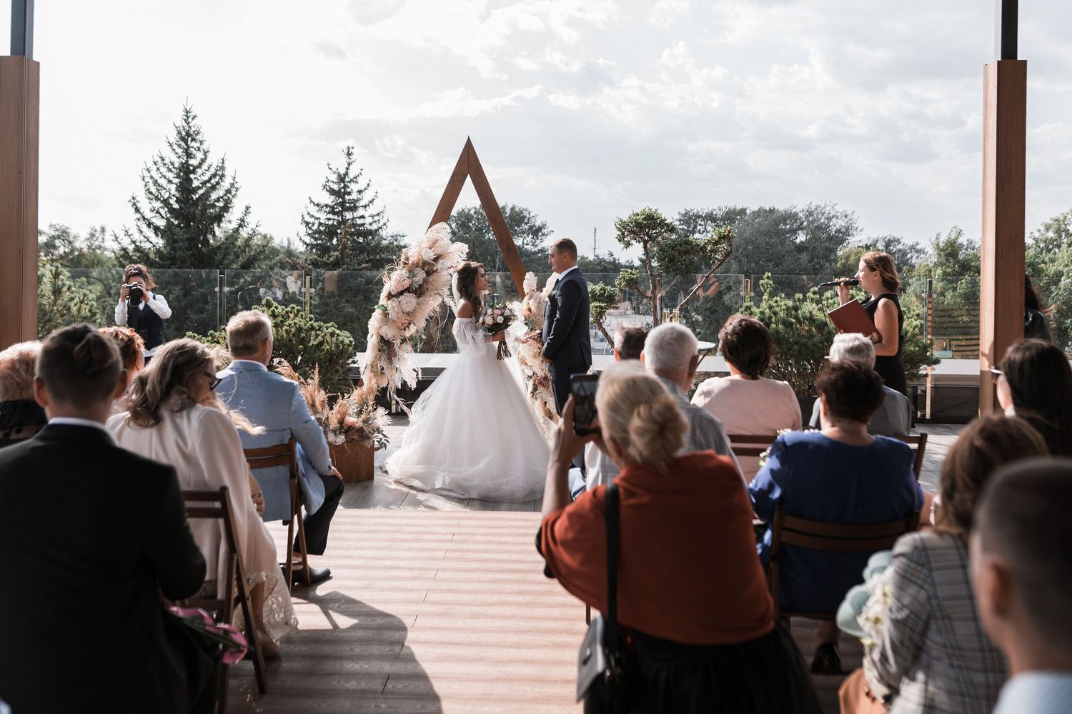 Wedding guests seated outdoors at a ceremony venue with mountains and evergreen trees in the scenic background.