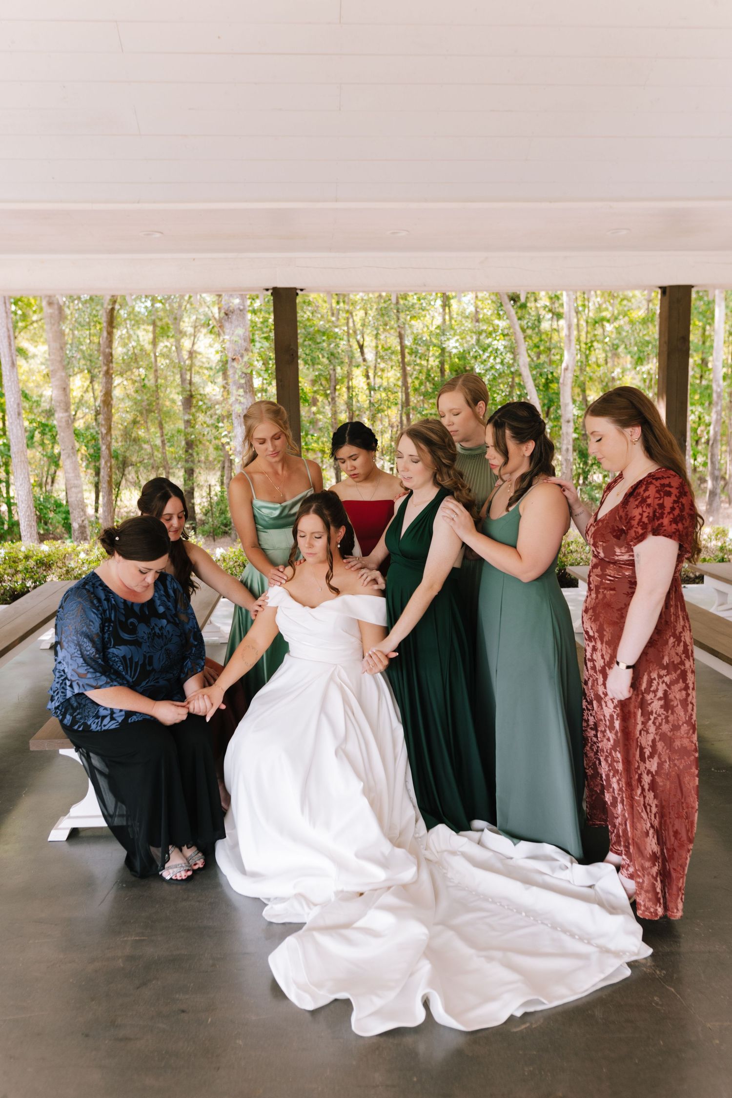 Wedding party in colorful dresses helping with the bride's gown outdoors.