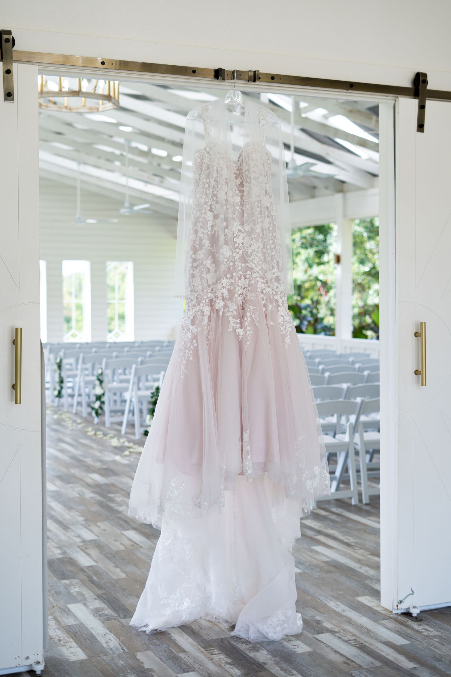 Delicate pink and white wedding gowns with lace details hang in an elegant white outdoor pavilion venue.