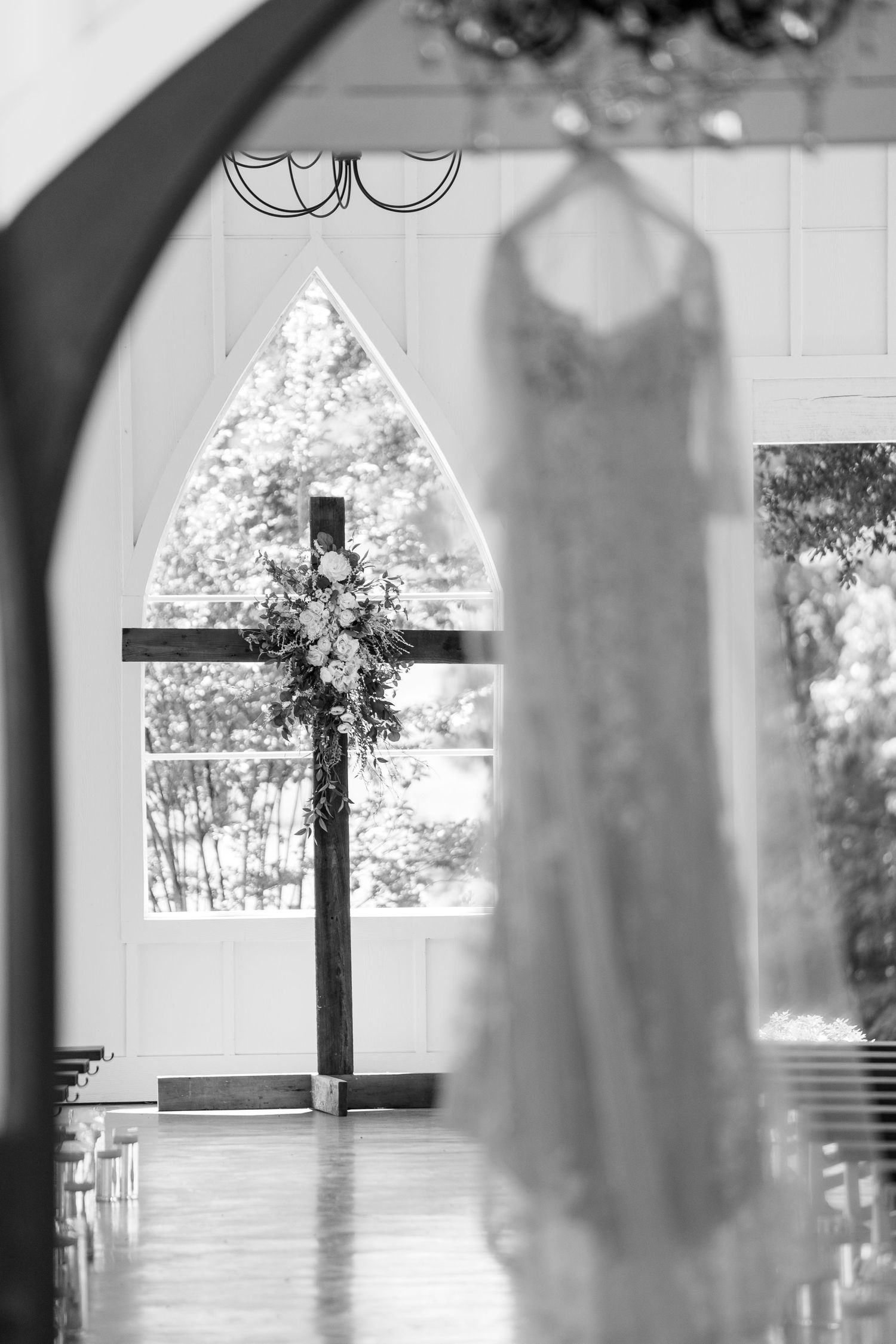 A silhouetted cross stands in front of an arched window inside a church sanctuary with soft natural lighting.