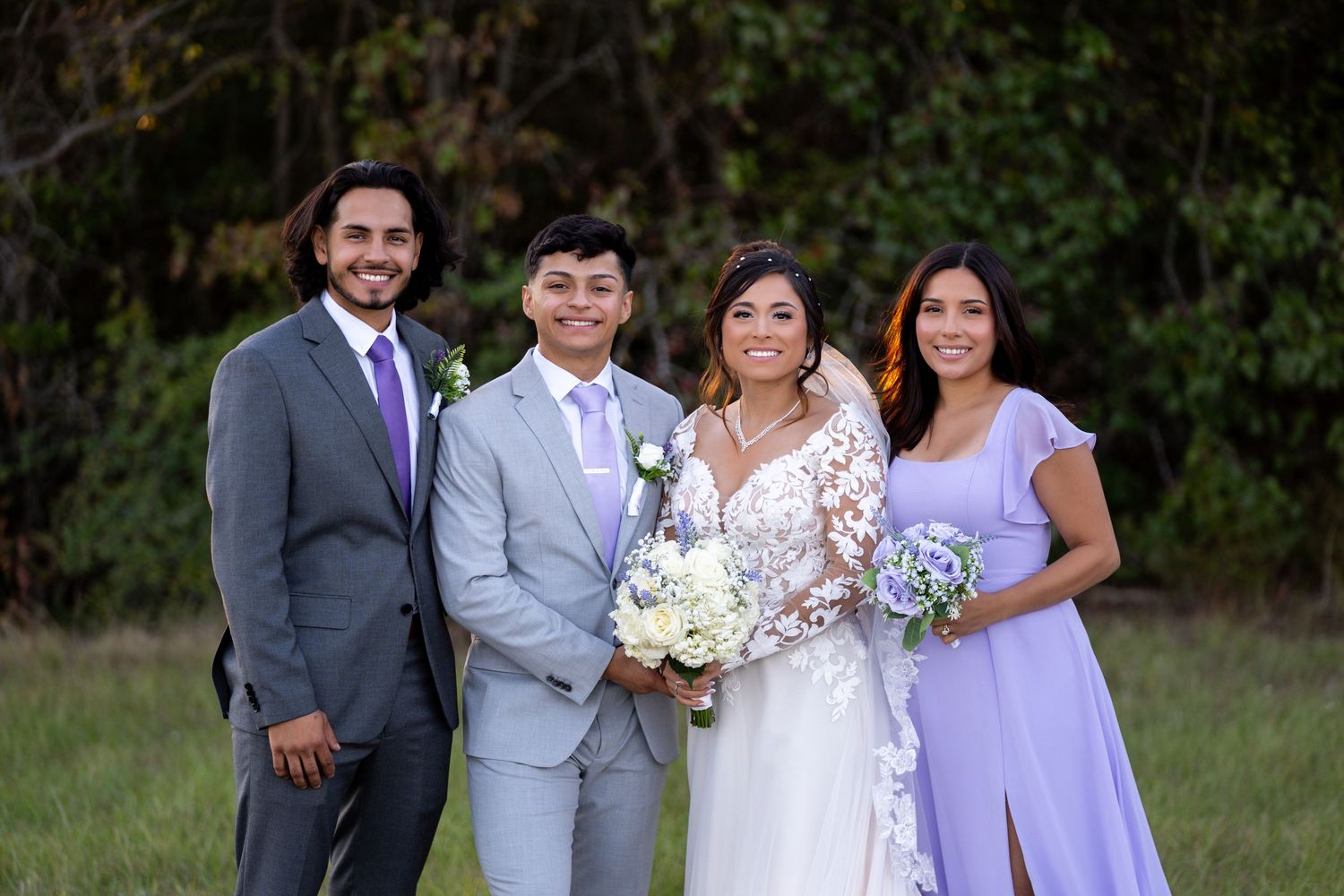 Wedding party in purple and gray attire posed together in natural outdoor setting.