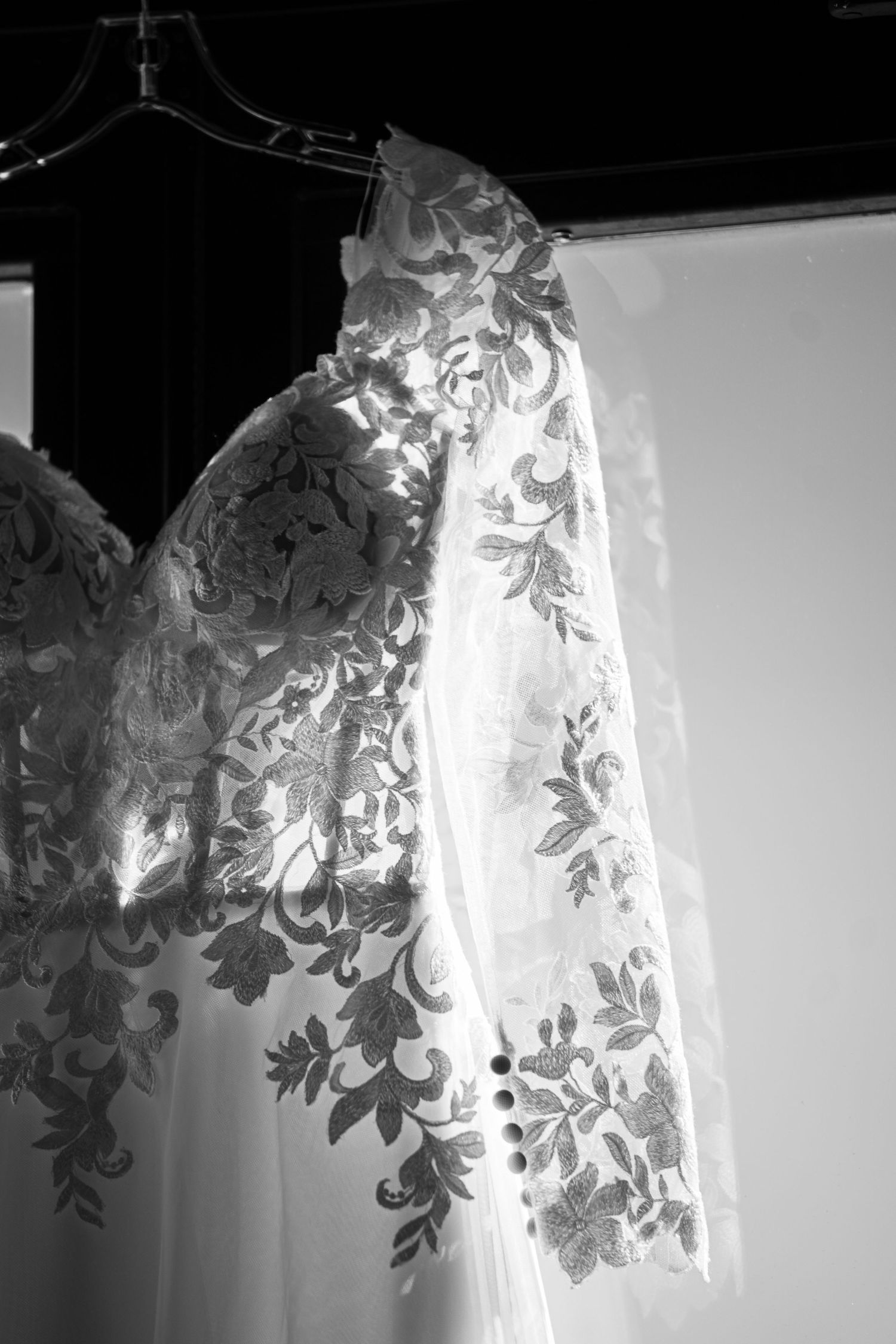 Black and white close-up of delicate floral lace details on wedding dress fabric.