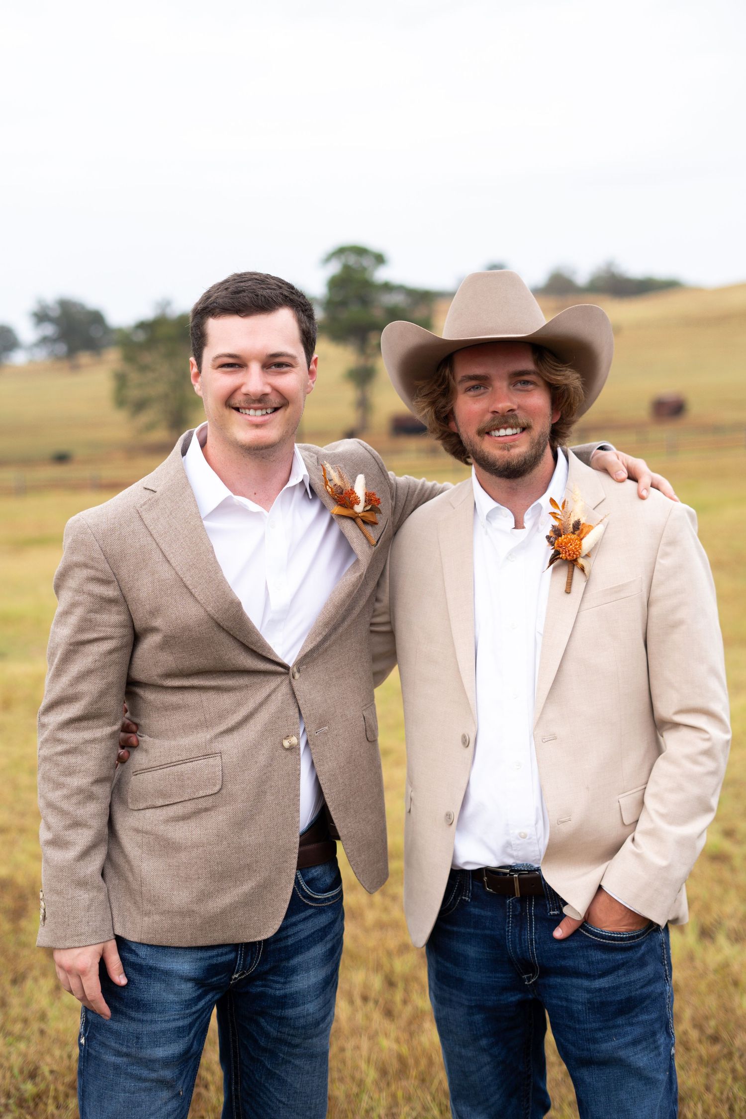 Groomsmen in tan blazers and cowboy hats smile together in a golden field.