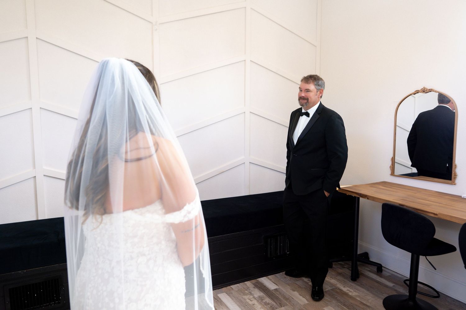 A wedding couple stands in front of a white wall while a photographer captures their special moment.