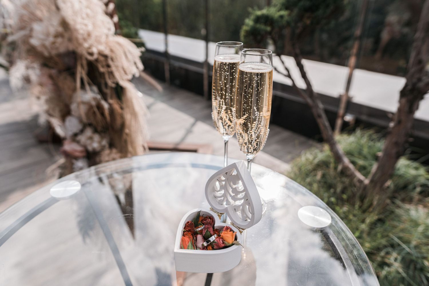 A glass of champagne and chocolate truffles on a round table with an outdoor garden view in the background.